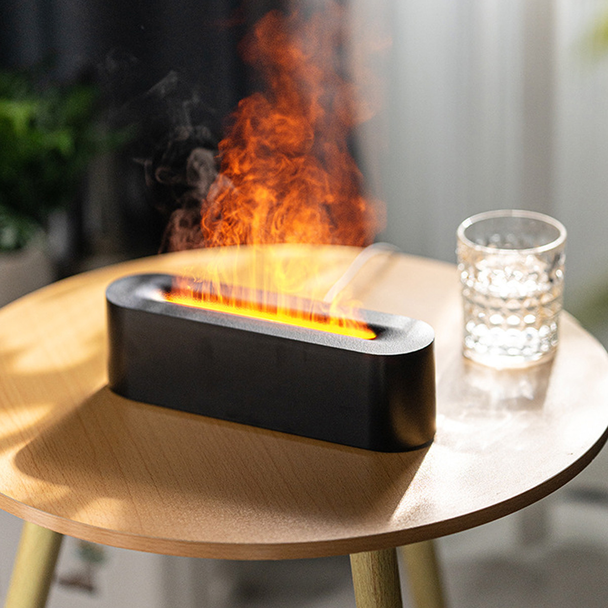 Ein dekoratives schwarzes Gerät mit Flammeneffekt steht auf einem Holztisch neben einem Wasserglas. Der Hintergrund ist unscharf.