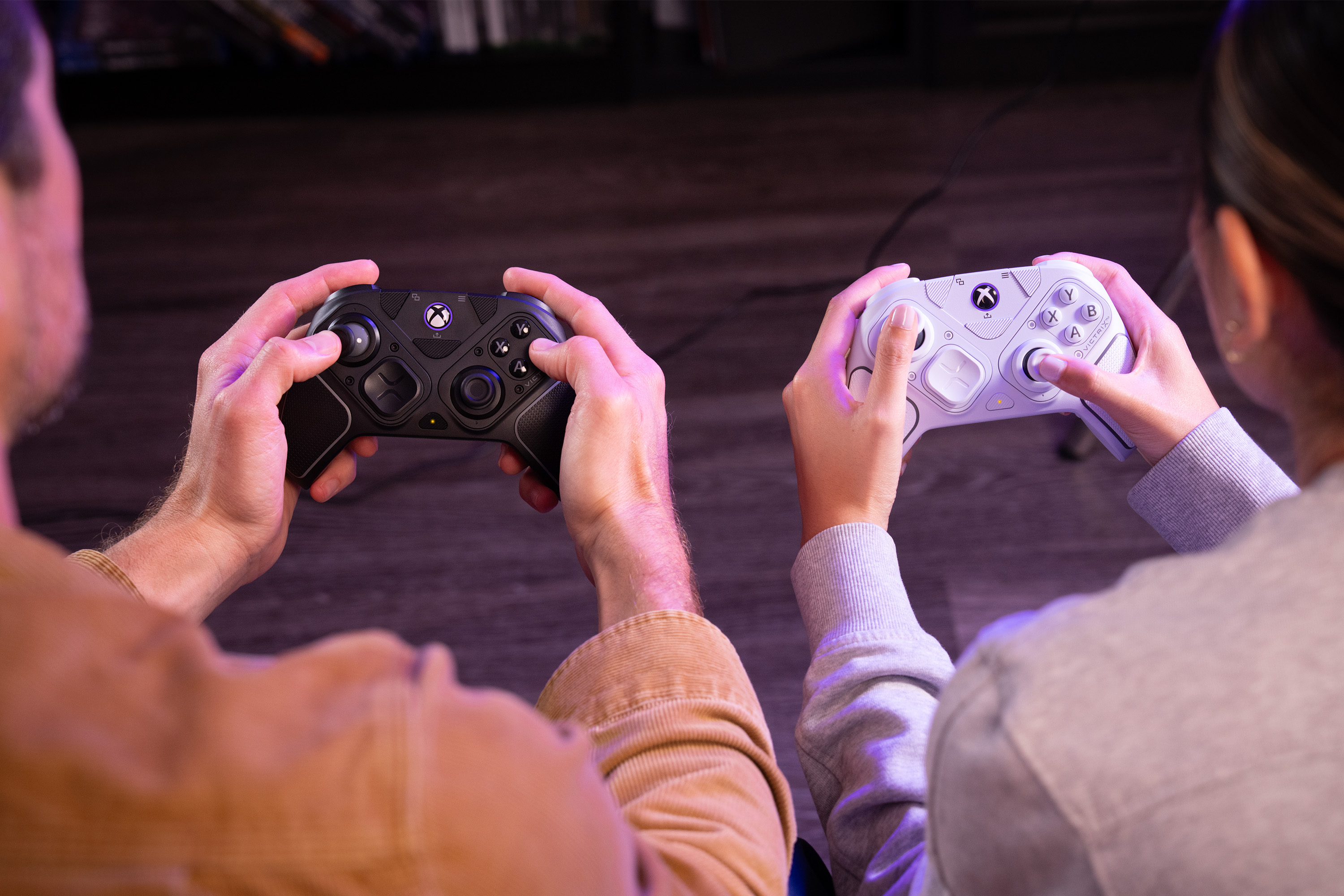 Zwei Personen halten Xbox-Controller, einen schwarzen, einen weißen, in einem schwach beleuchteten Raum.