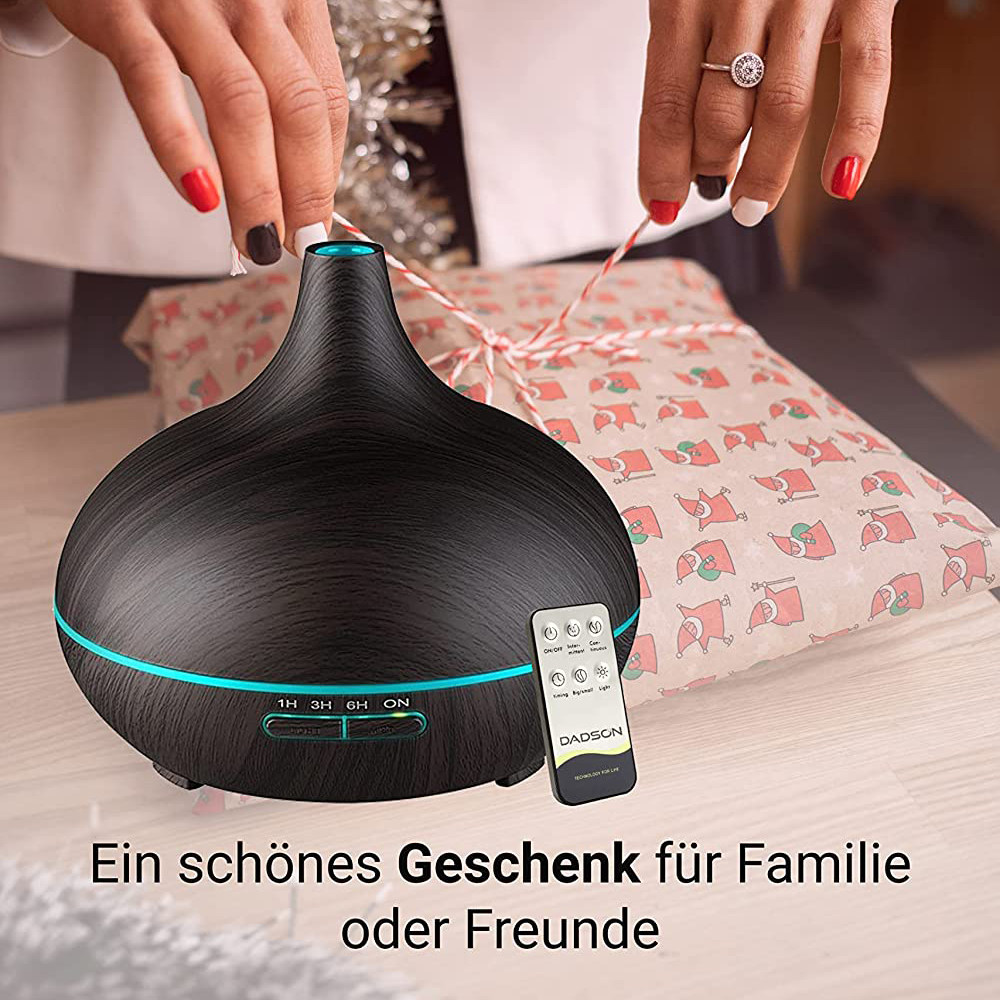 Ein schwarzer Diffusor mit Fernbedienung, Hände mit lackierten Nägeln und ein Geschenk in Weihnachtspapier verpackt.