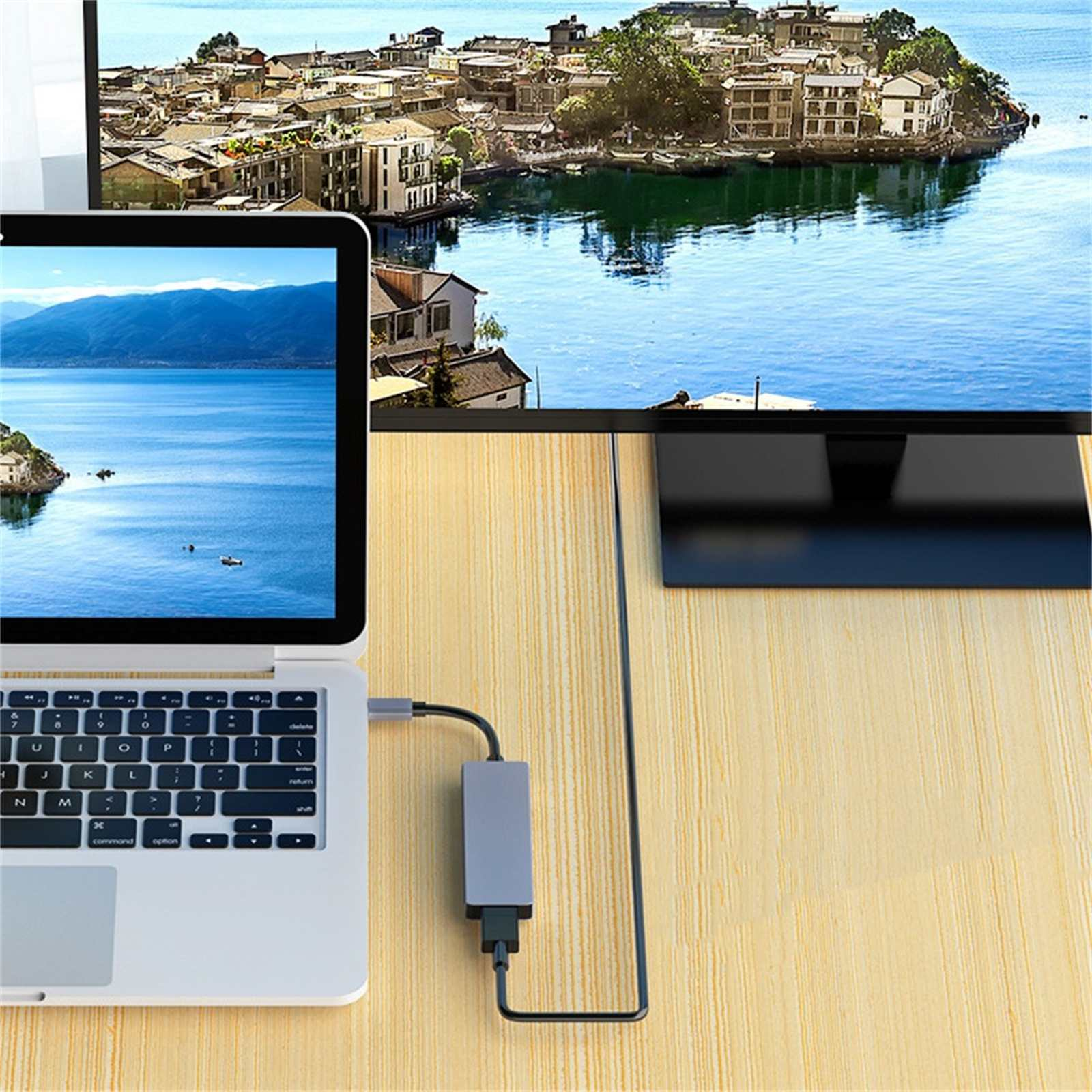 Laptop ist mit einem Monitor verbunden, der eine malerische Aussicht zeigt. Kabel und Adapter sind sichtbar. Die Szene ist auf Holz.