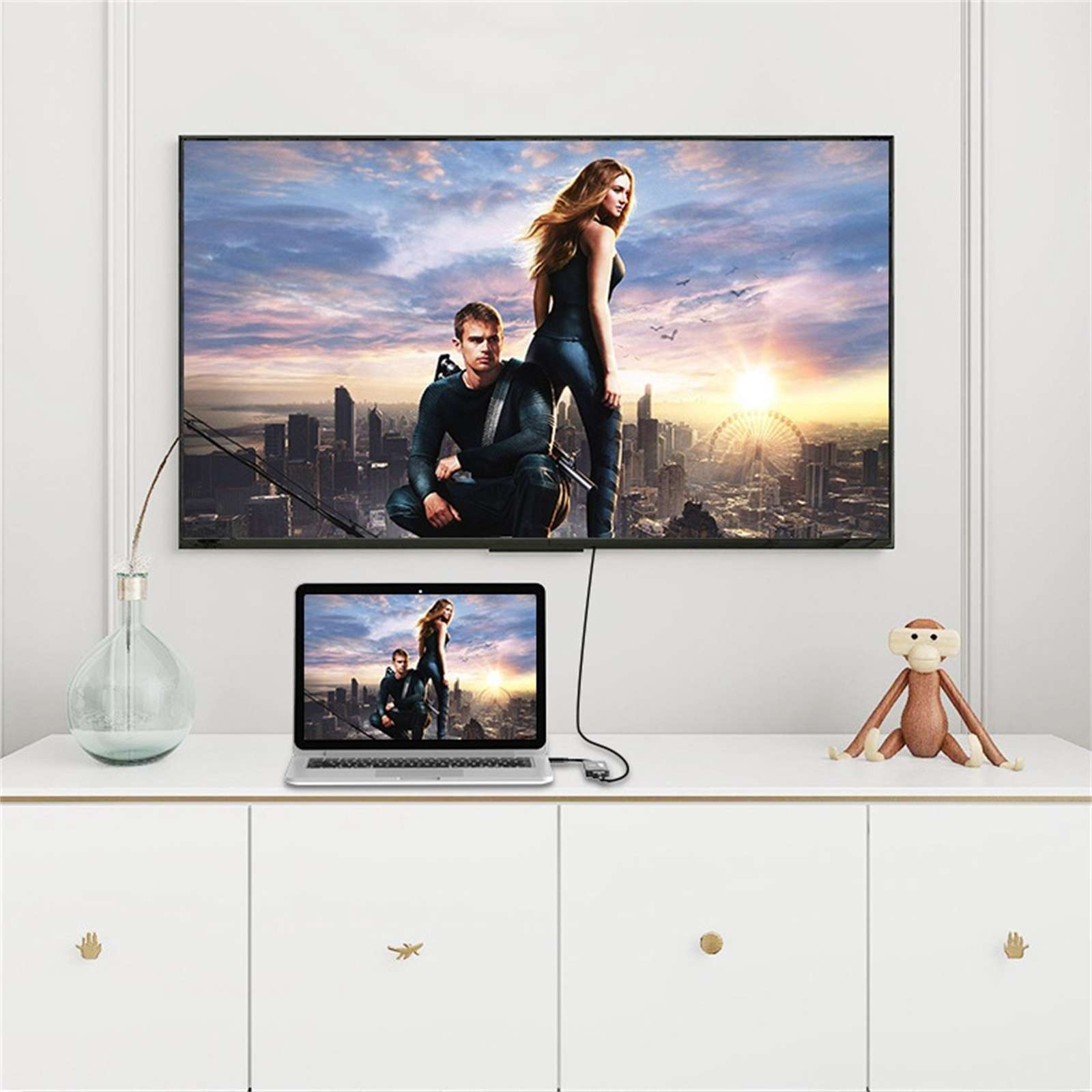 Ein Fernseher und ein Laptop zeigen eine Filmszene. Ein Affenspielzeug sitzt auf dem weißen Schrank unter den Bildschirmen.