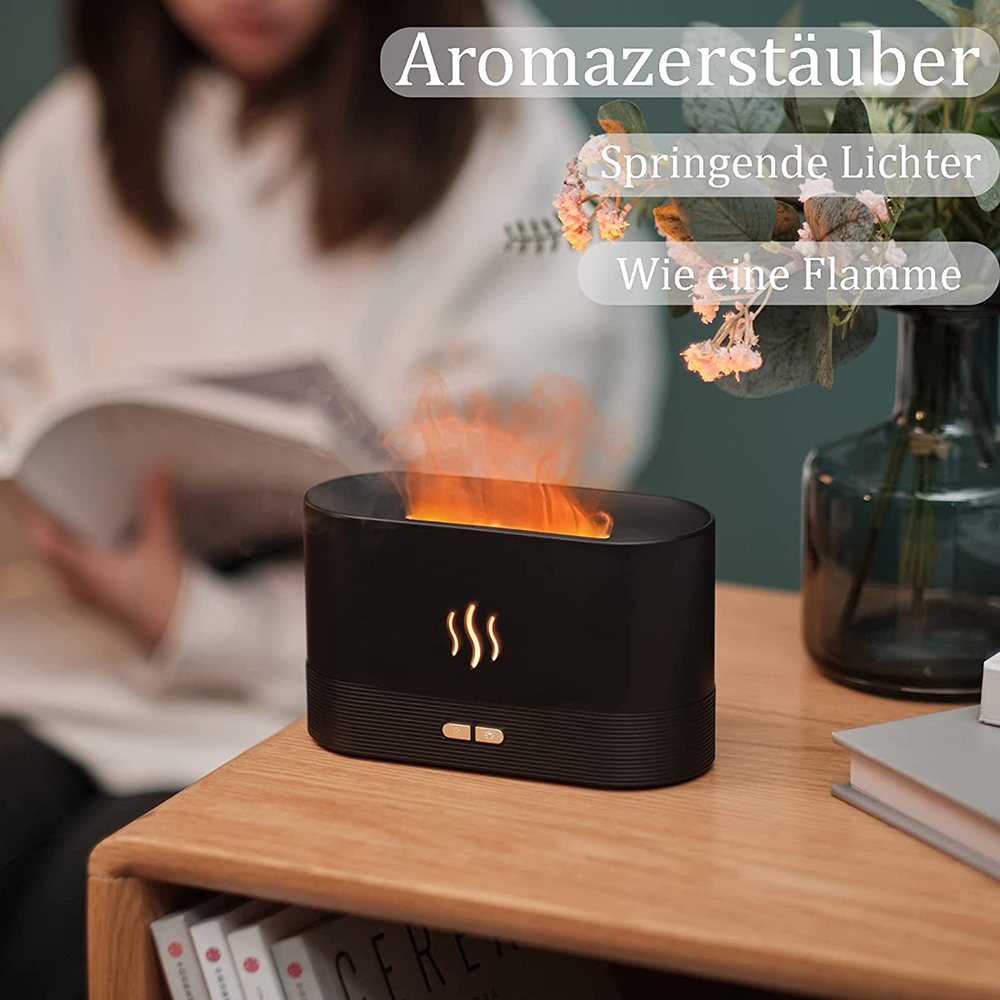Ein schwarzer Aromadiffusor mit flammenartigem Dampf steht auf Holz. Eine Person liest im unscharfen Hintergrund. Blumen und Bücher sind ebenfalls vorhanden.