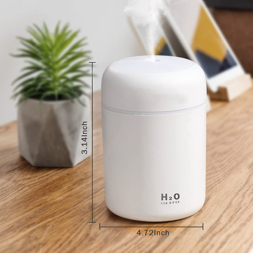 Ein weißer H2O-Luftbefeuchter mit Dampf, eine kleine Pflanze und eine Holzoberfläche. Abmessungen: 3,14 Zoll Höhe, 4,72 Zoll Breite.