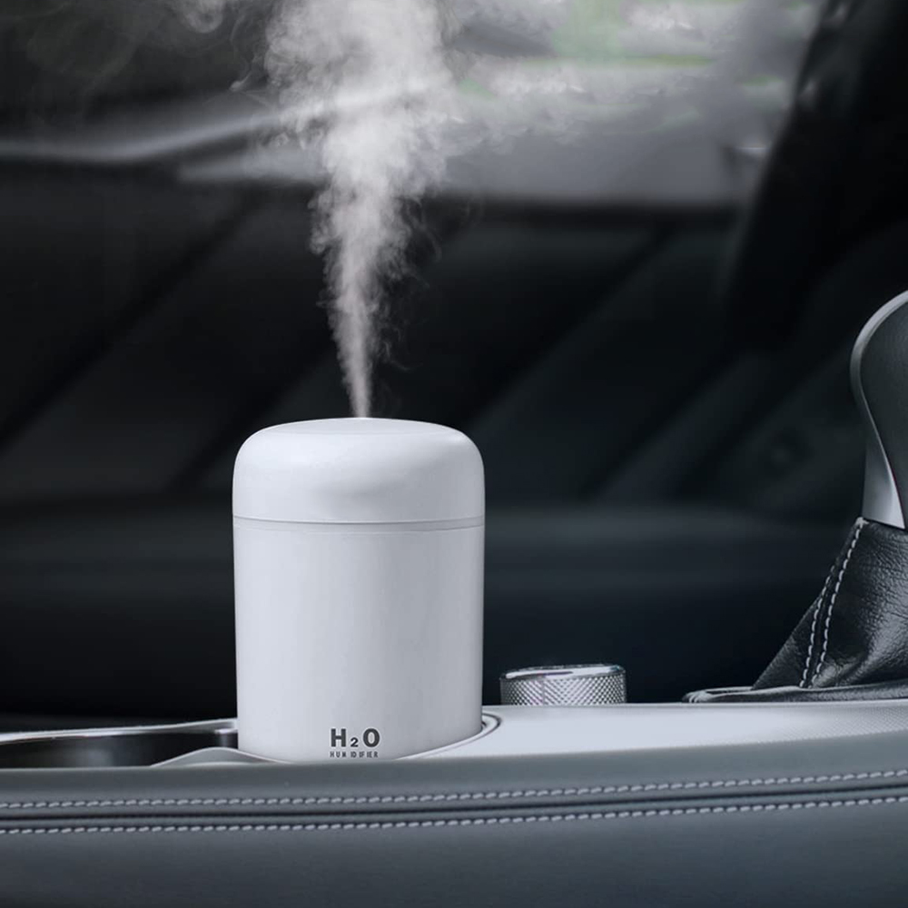 Ein weißer Luftbefeuchter in einem Autobecherhalter gibt Dampf ab. Der Innenraum des Autos ist dunkelgrau mit Lederdetails.