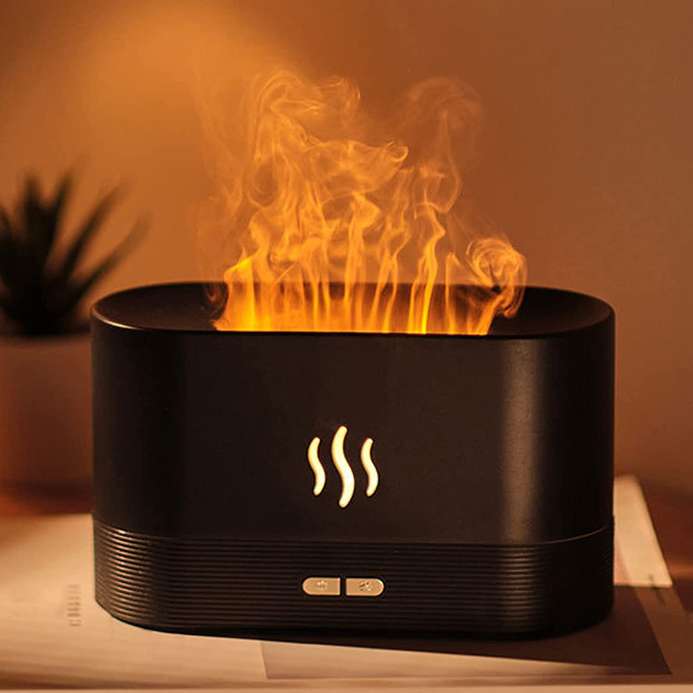 Ein schwarzer Luftdiffusor mit Flammeneffekt und dampfartiger Flamme. Es hat ein Flammensymbol und Steuertasten auf einem Tisch. Im Hintergrund eine Pflanze.