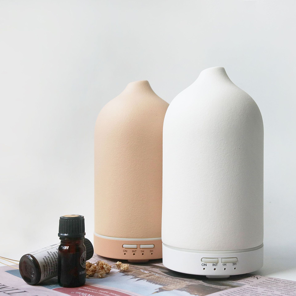 Zwei Keramik-Aromadiffusoren, einer beige, einer weiß. Kleine Flaschen ätherischen Öls davor. Trockenblumen und eine Zeitschrift sind vorhanden.