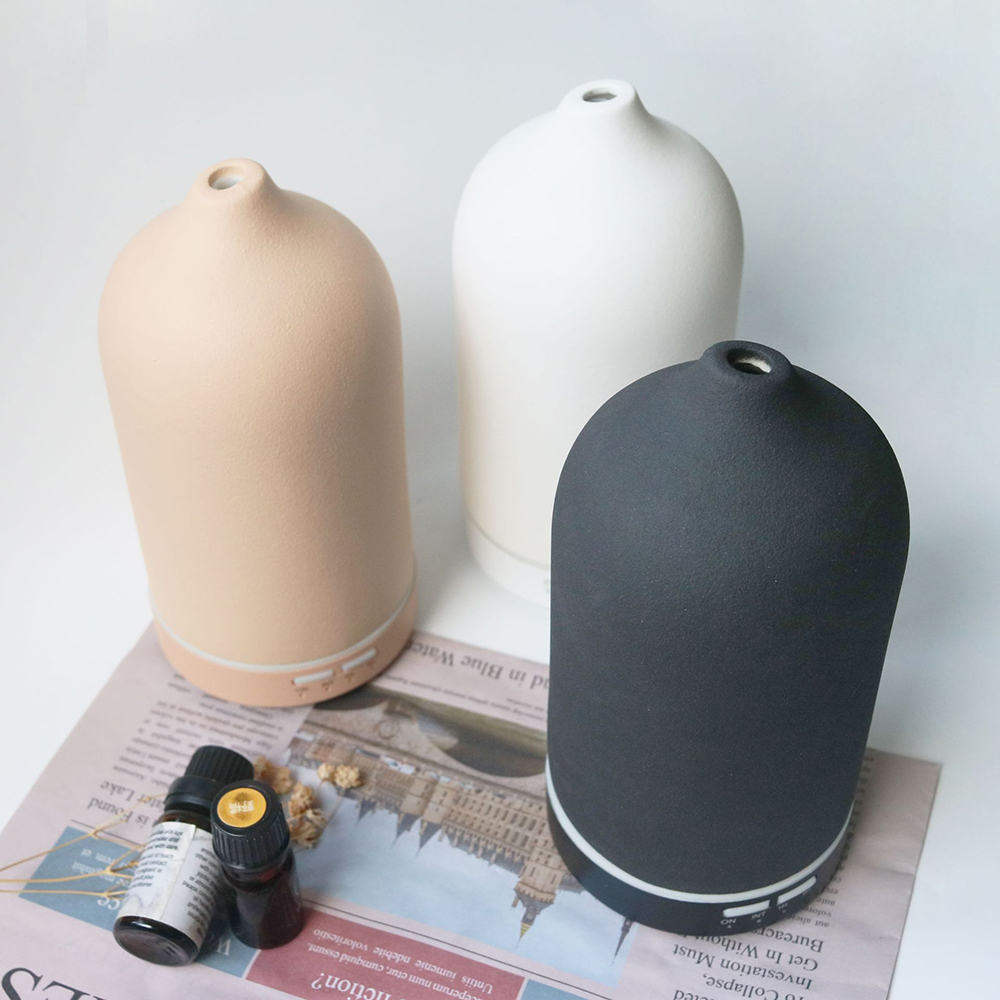 Drei Keramikdiffusoren in Beige, Weiß und Schwarz stehen auf einer Zeitung. Kleine ätherische Ölflaschen sind im Vordergrund.