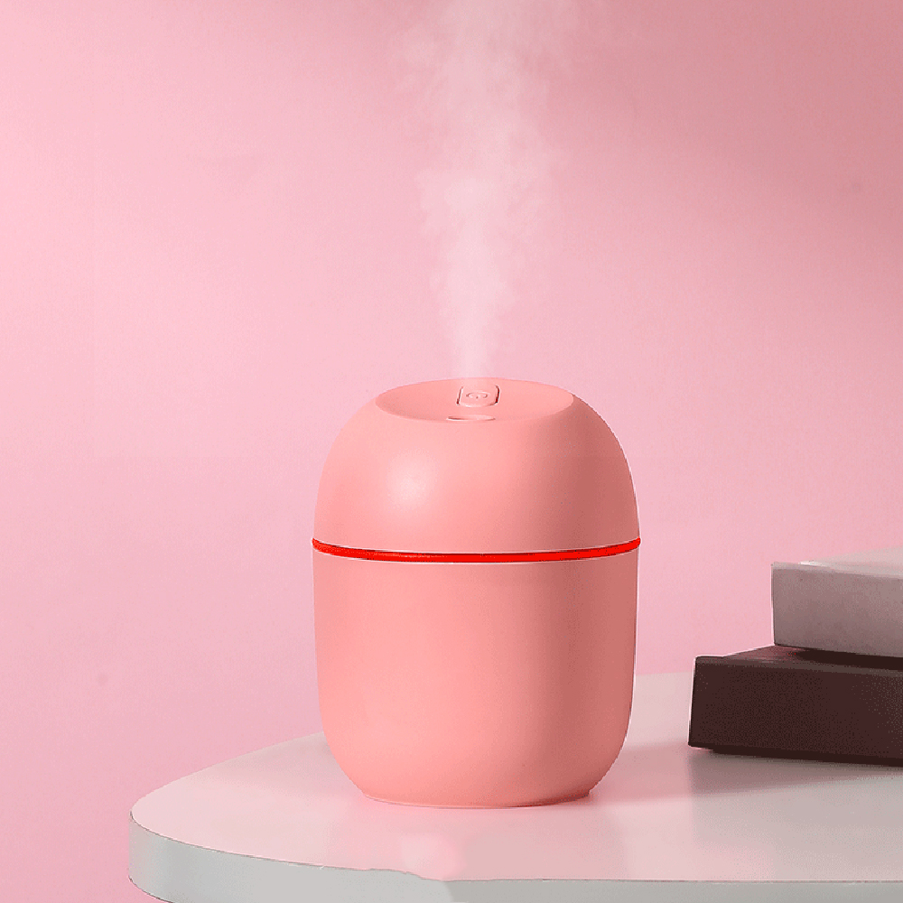 Ein rosa Luftbefeuchter mit rotem Streifen steht auf einem weißen Tisch. Dampf steigt vor rosa Hintergrund auf. Bücher sind im Hintergrund.