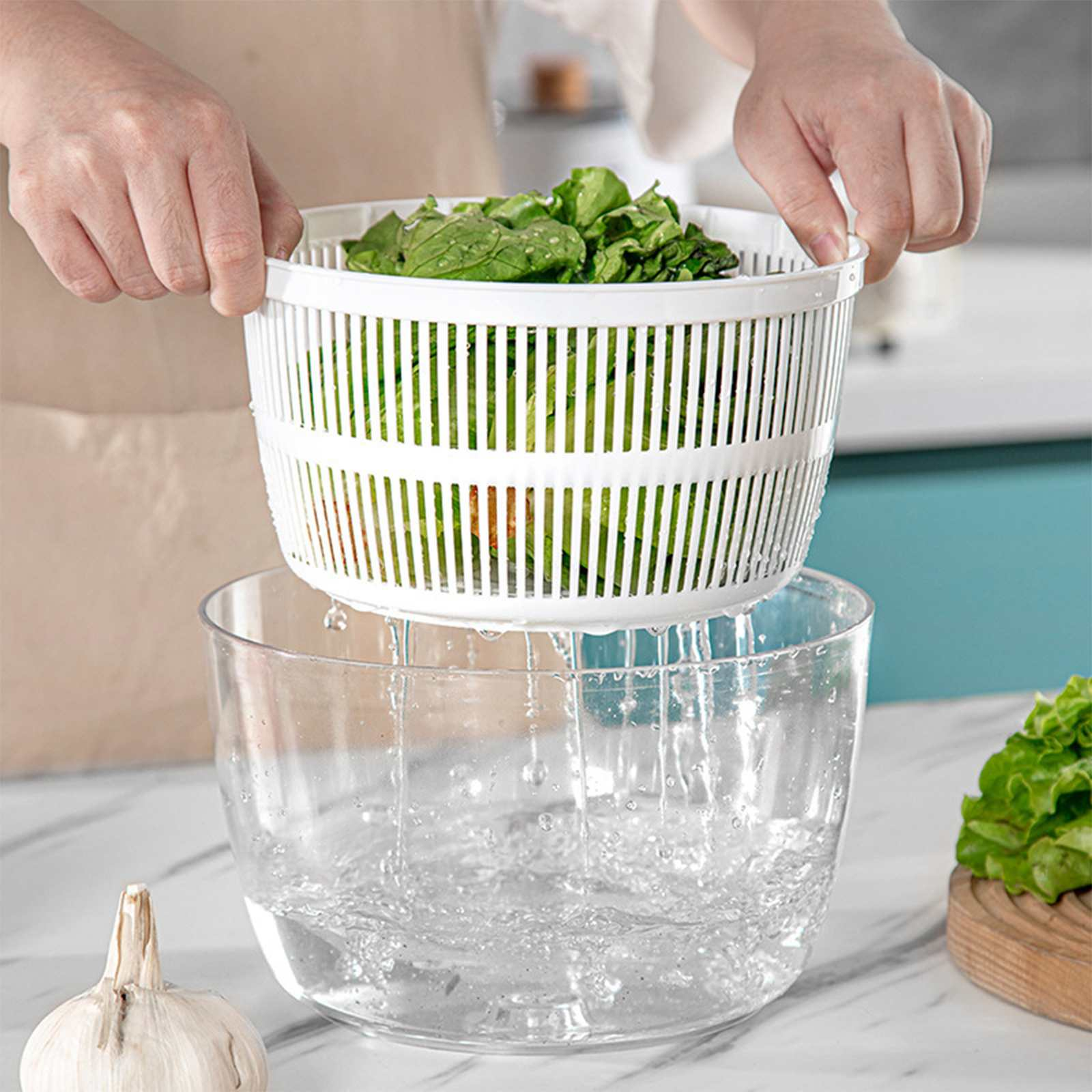 Hände halten eine weiße Salatschleuder mit grünem Salat über einer klaren Wasserschüssel.