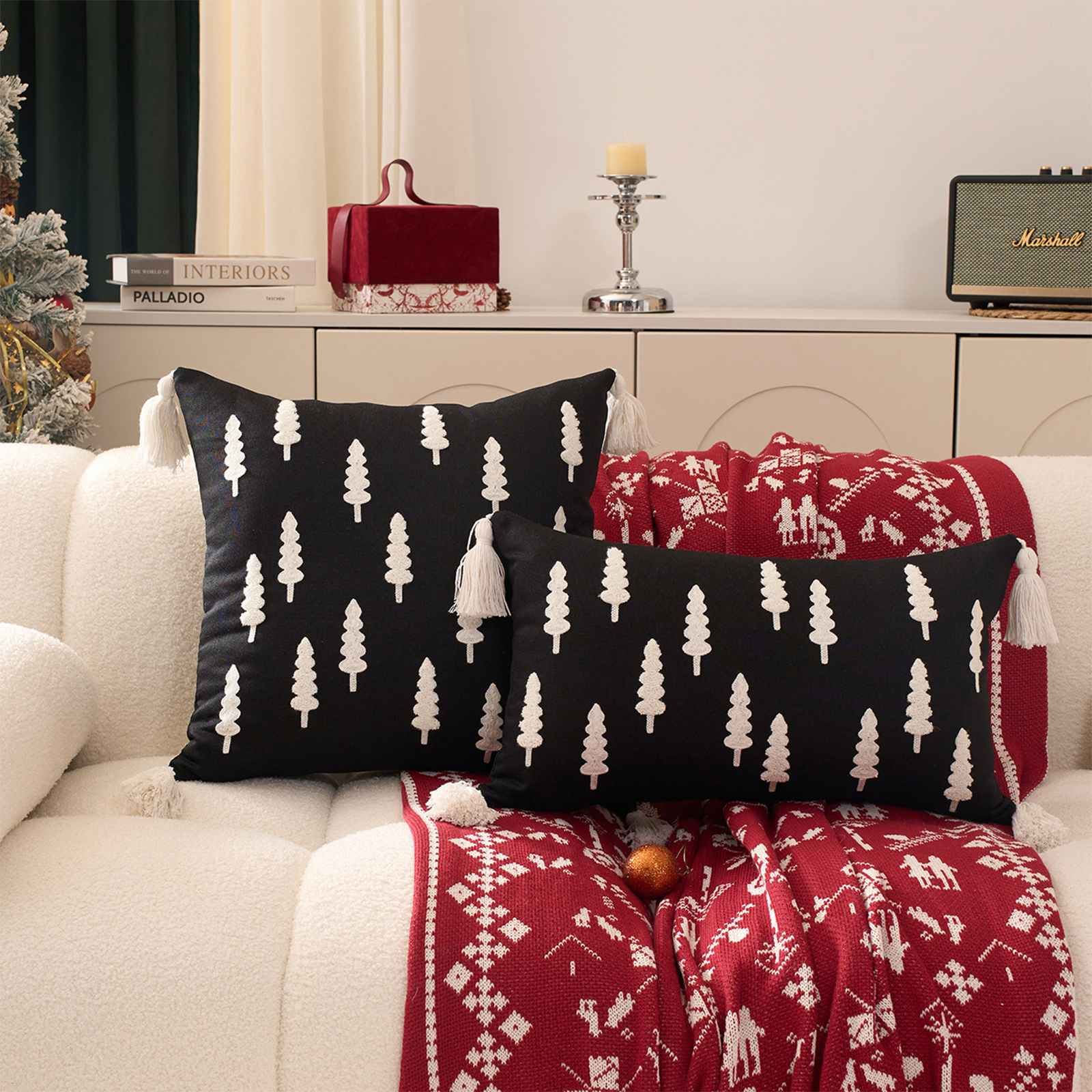 Wohnzimmerszene mit weißem Sofa, schwarzen Kissen mit Baummustern und einer roten Decke mit weißen Mustern.