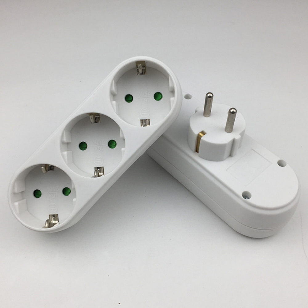 Zwei weiße elektrische Adapter auf weißem Untergrund. Einer hat drei Steckdosen, der andere einen Stecker. Grüne Punkte sind in den Steckdosen zu sehen.
