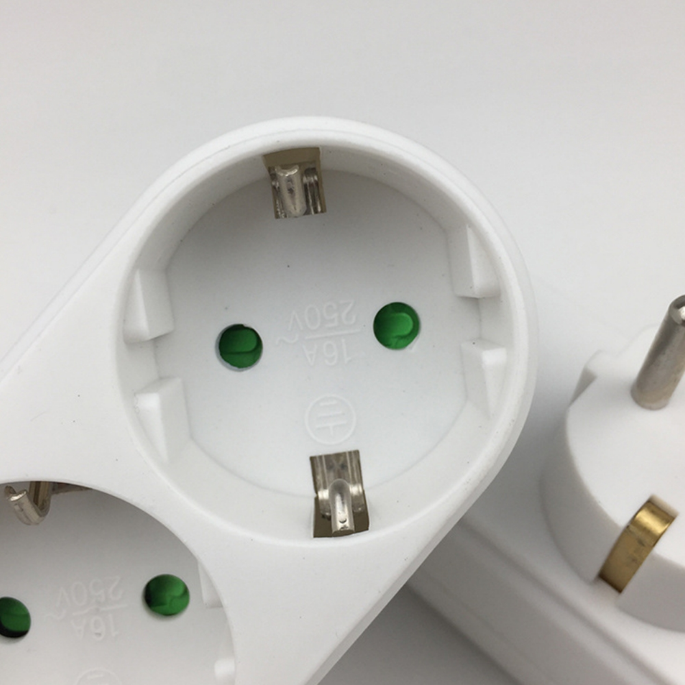 Nahaufnahme einer weißen Steckdosenleiste mit drei Steckdosen und einem Stecker. Jede Steckdose hat grüne Löcher und Metallanschlüsse. Weißer Hintergrund.