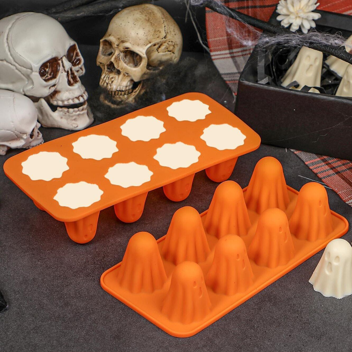 Halloween-Szene mit orangefarbenen Geisterformen und Totenköpfen. Ein Geist ist außerhalb der Form. Weiße Geisterbonbons in einer Schachtel.