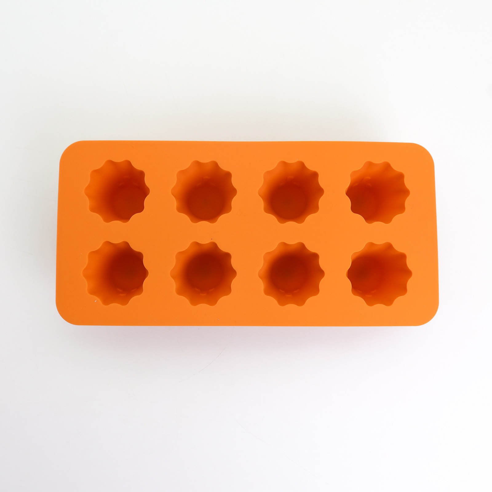 Eine orangefarbene Silikonform mit acht blumenförmigen Hohlräumen auf weißem Untergrund. Die Form ist rechteckig.