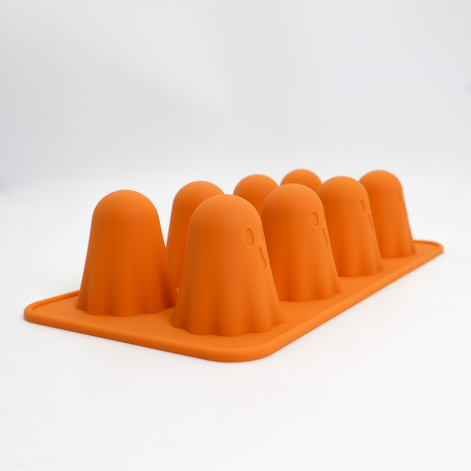 Orangene Silikonform mit Geisterformen. Jeder Geist hat kleine Augen- und Mundvertiefungen. Weißer Hintergrund.