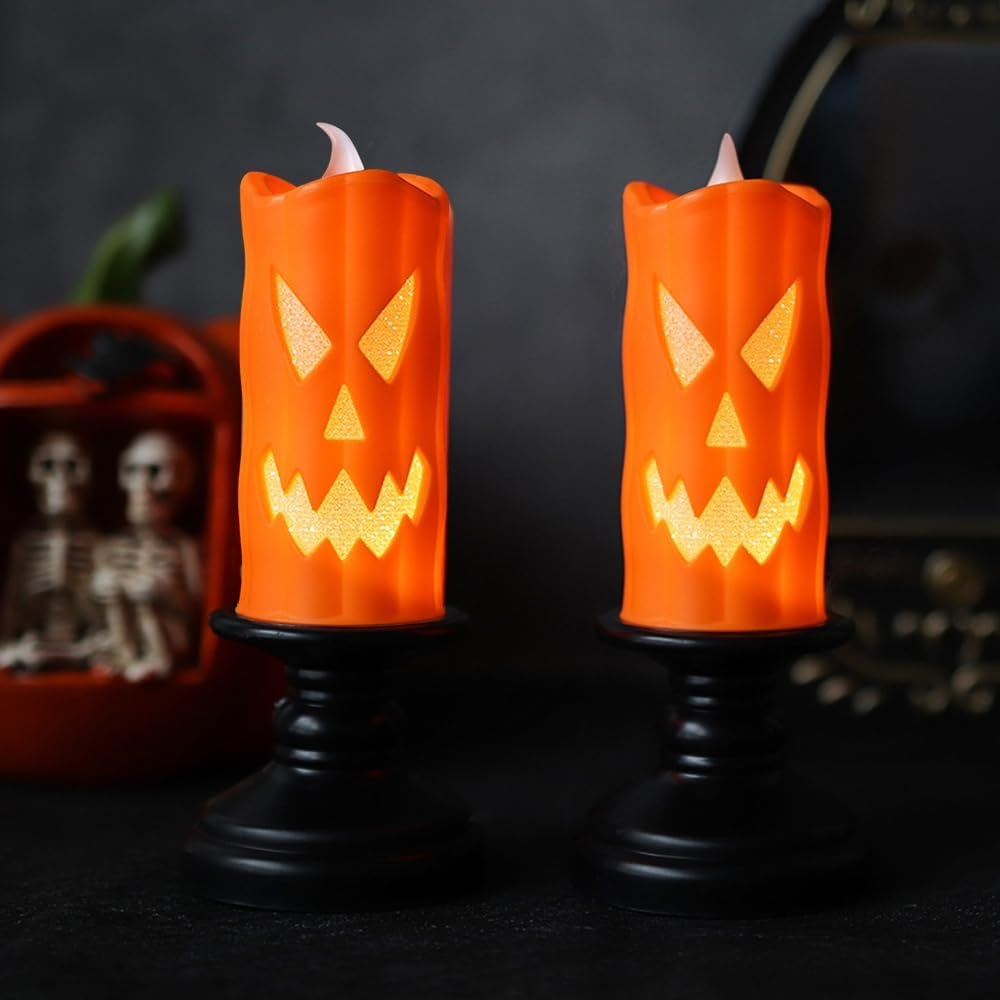 Zwei orangefarbene Kerzen mit Kürbisgesicht auf schwarzen Ständern, mit einem Kürbisgesicht und Skeletten im Hintergrund.