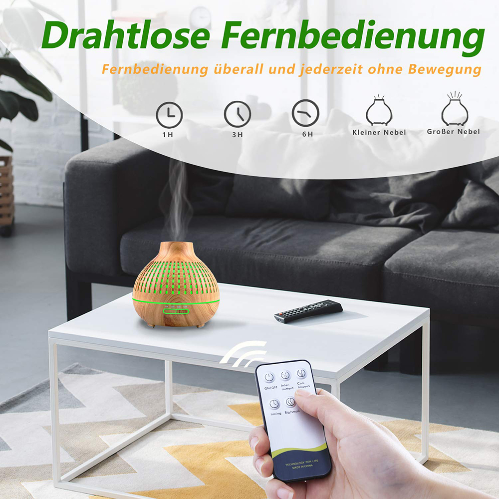Eine Hand hält eine Fernbedienung, die auf einen Aromadiffusor auf einem weißen Tisch zeigt. Der Diffusor stößt Dampf aus. Im Hintergrund ist eine Couch.