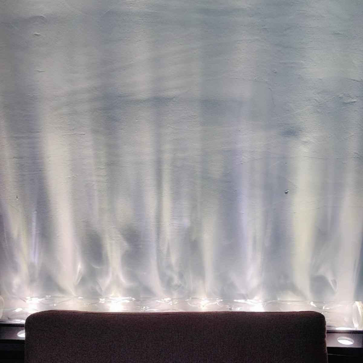 Eine Wand mit wellenförmigen Lichtreflexen. Unten befindet sich ein dunkelbrauner Sitz. Das Licht sieht aus wie ein Wasserfall.
