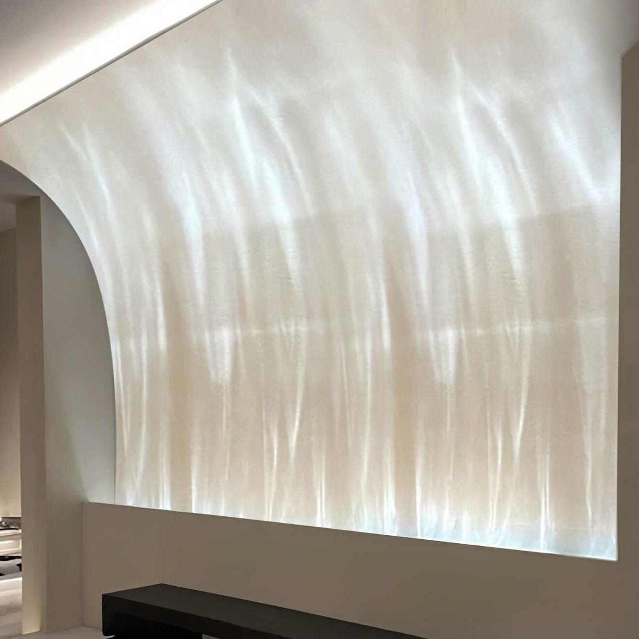 Eine weiße Wand mit Lichtmustern. Im Vordergrund befindet sich eine dunkle Bank. Die Wand hat einen gebogenen Abschnitt.