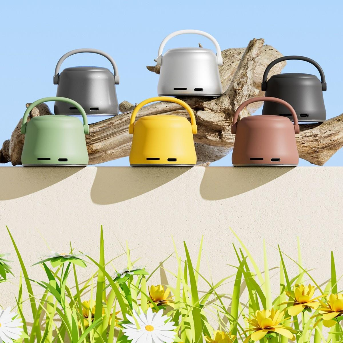 Sechs bunte Geräte mit Griff auf einem Holzstück. Darunter eine Wand mit Gras, Blumen und blauem Himmel im Hintergrund.