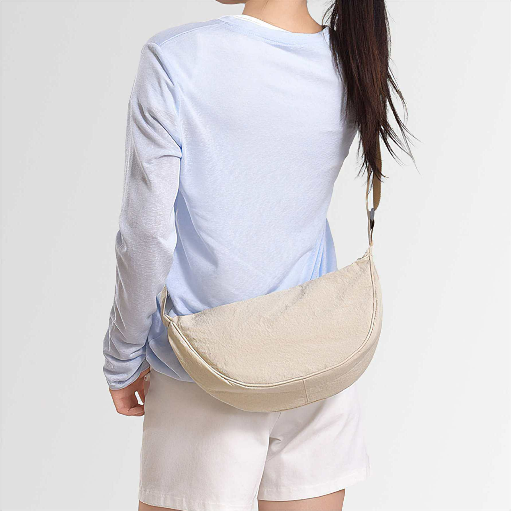 Eine Person von hinten, die ein hellblaues Hemd, weiße Shorts und eine beige halbmondförmige Tasche trägt.
