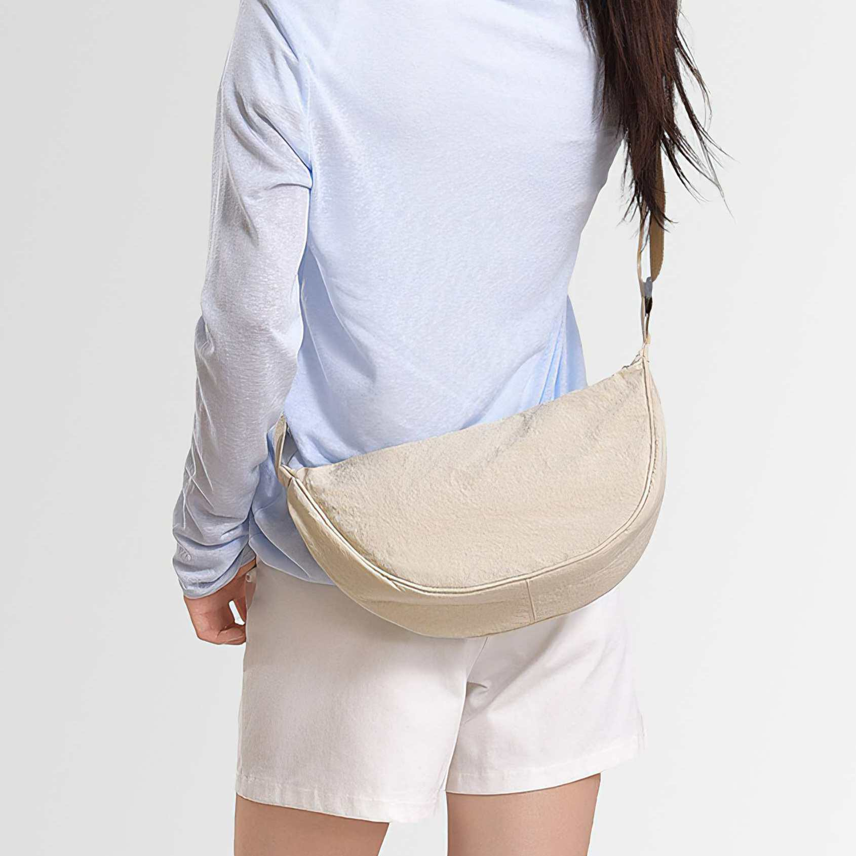 Eine Person trägt ein hellblaues Hemd, weiße Shorts und eine beige halbmondförmige Tasche.
