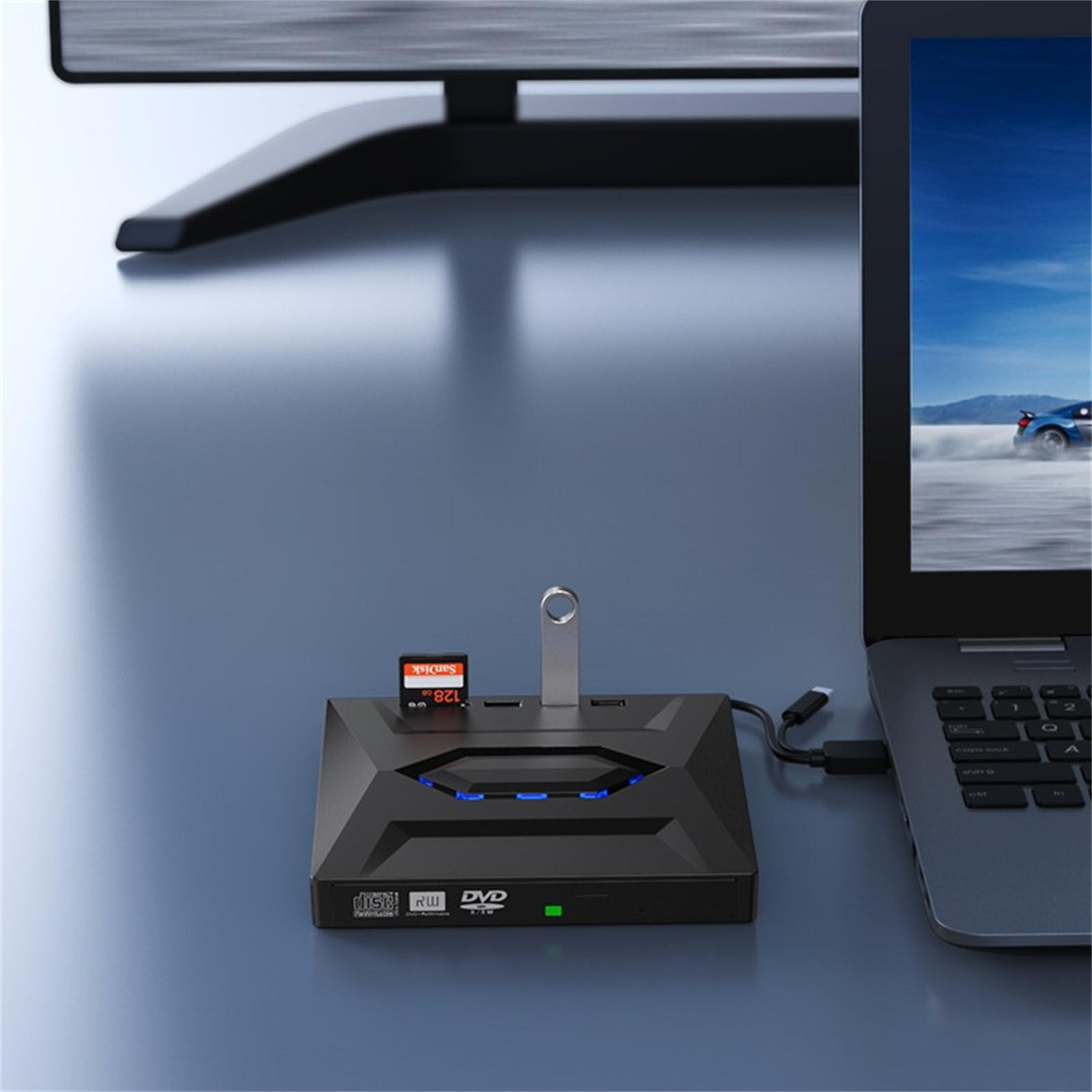 Schwarzer USB-Hub, SD-Kartenleser und Laptop. Der Laptop zeigt ein Auto auf einer Rennstrecke. Ein Monitor im Hintergrund.