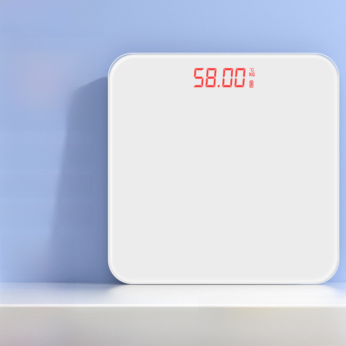 Eine weiße Digitalwaage zeigt '58.00' an. Sie steht auf einer weißen Oberfläche vor einer blauen Wand. Die Waage hat abgerundete Ecken.