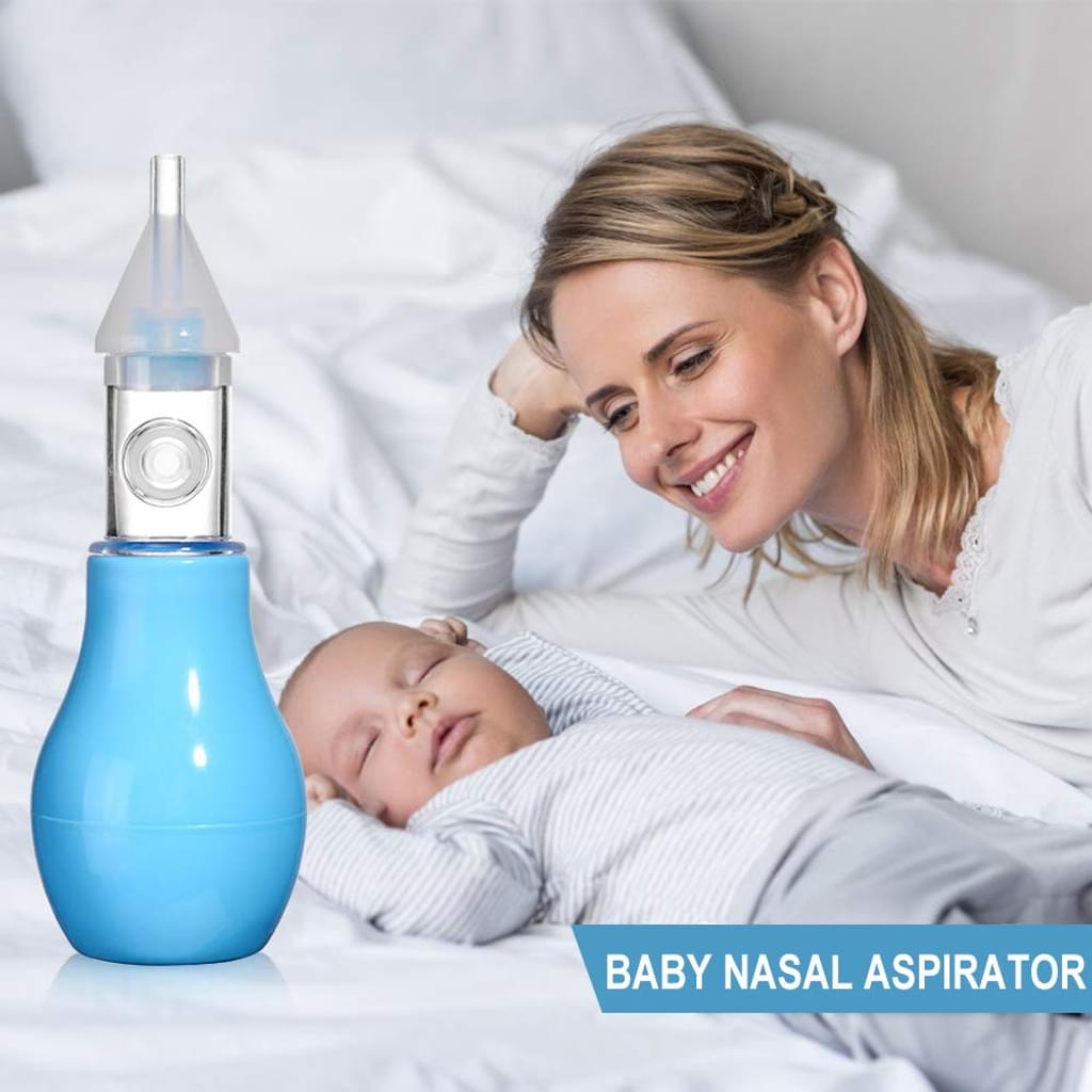 Ein Baby schläft neben einem blauen Nasensauger auf einem Bett. Eine Frau lächelt und betrachtet das Baby.