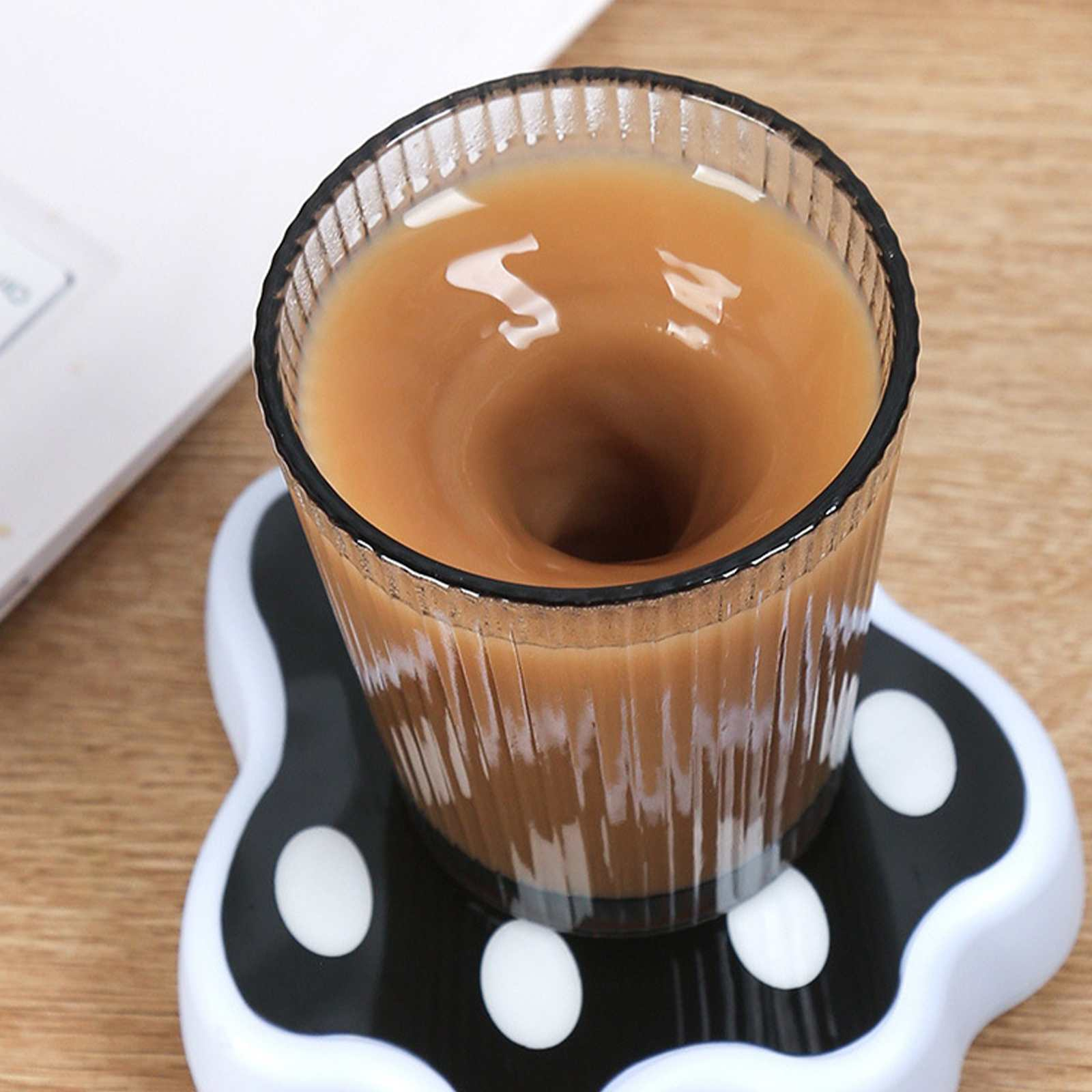 Ein Glas Kaffee wirbelt auf einem pfotenförmigen Untersetzer. Das Getränk ist braun, der Untersetzer schwarz-weiß.