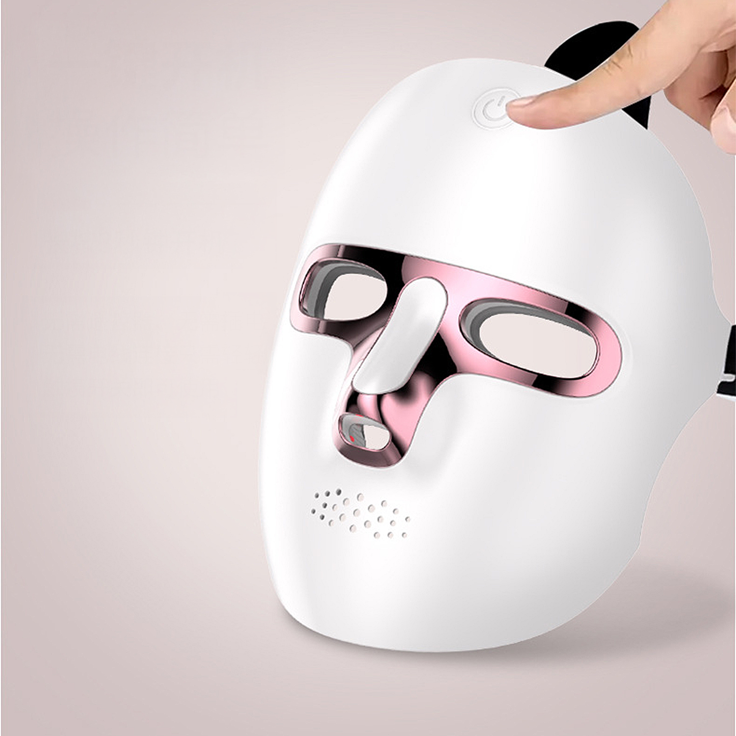 Eine weiße LED-Gesichtsmaske mit rosa Akzenten wird gehalten. Ein Finger drückt den Einschaltknopf. Der Hintergrund ist ein sanfter rosa Farbverlauf.