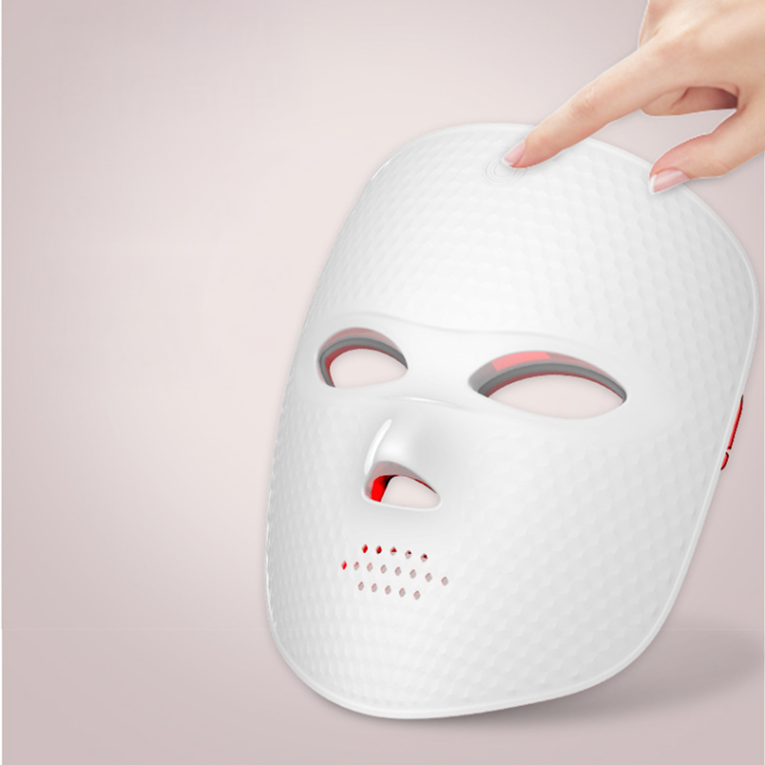 Eine weiße LED-Gesichtsmaske mit einer Hand, die einen Knopf oben drückt. Die Maske hat rote Lichter und eine strukturierte Oberfläche.