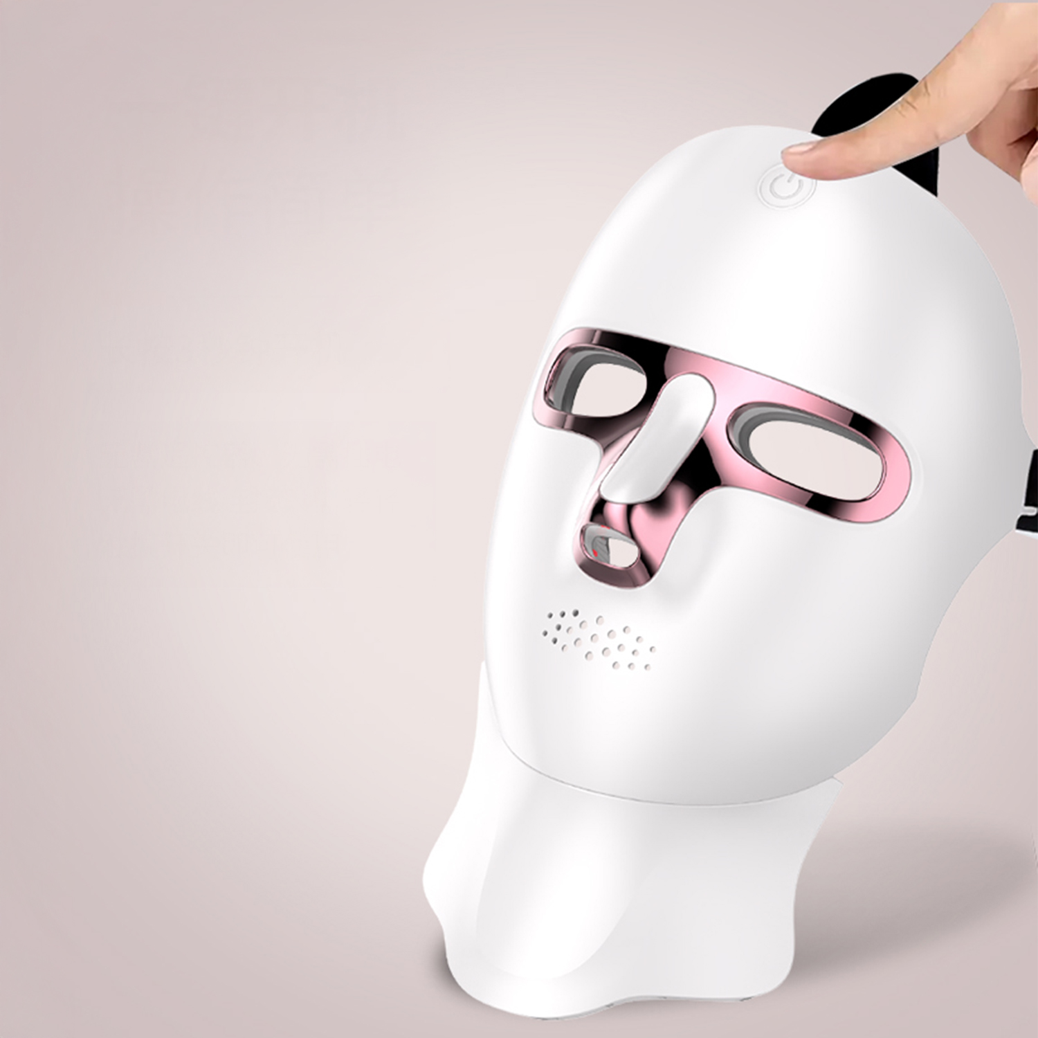 Maschera per il viso bianca con dettagli rosa. Un dito preme il pulsante di accensione. Lo sfondo è un rosa chiaro sfumato.