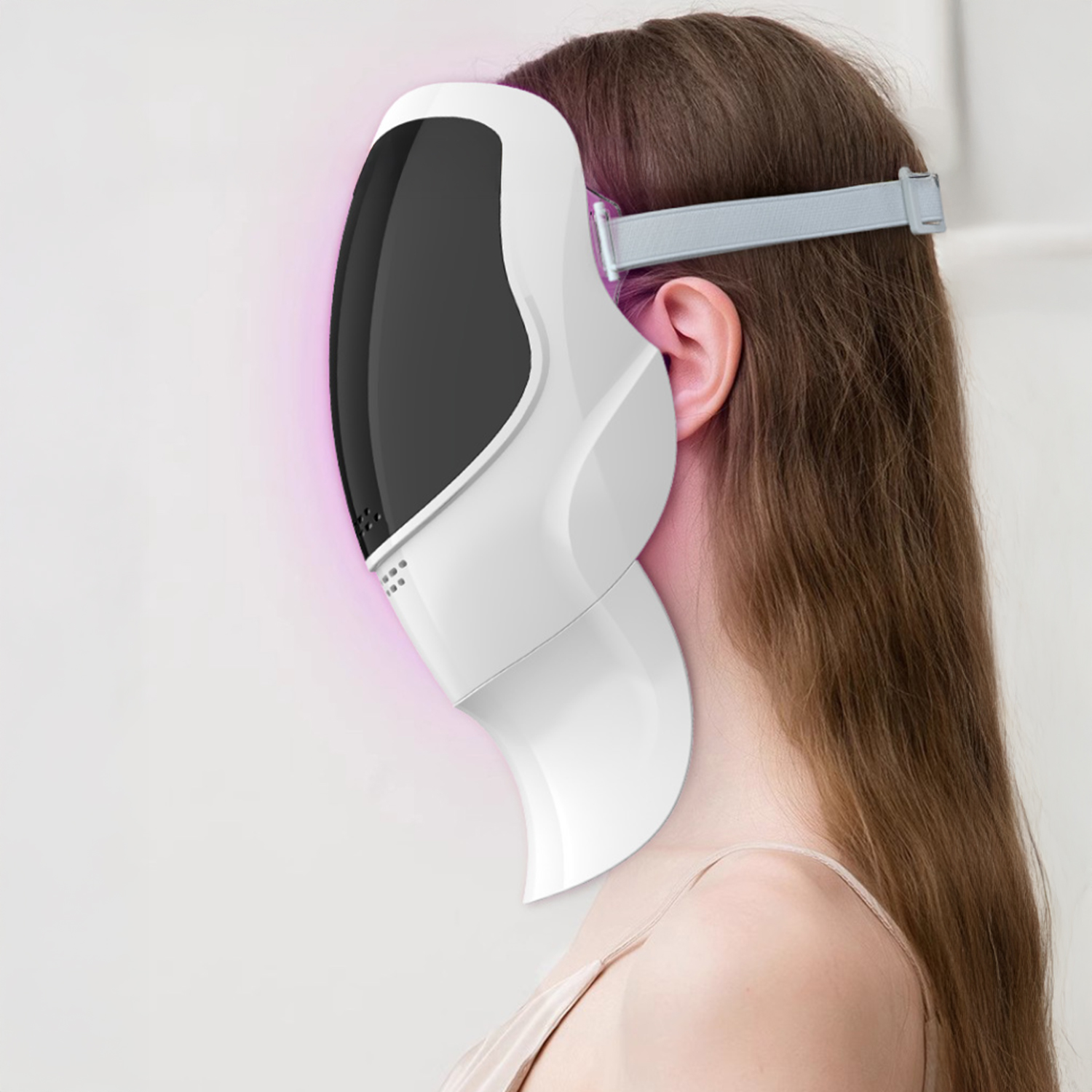 Eine Frau trägt eine weiße LED-Gesichtsmaske. Ihr braunes Haar ist offen. Ein rosa Leuchten ist sichtbar. Weißer Hintergrund.