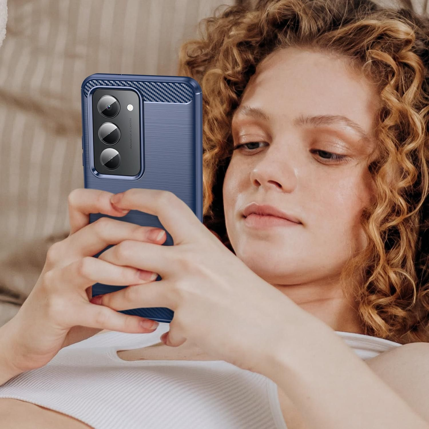 Una mujer con cabello rizado sostiene un teléfono azul. Está mirando la pantalla. La funda del teléfono tiene tres cámaras.