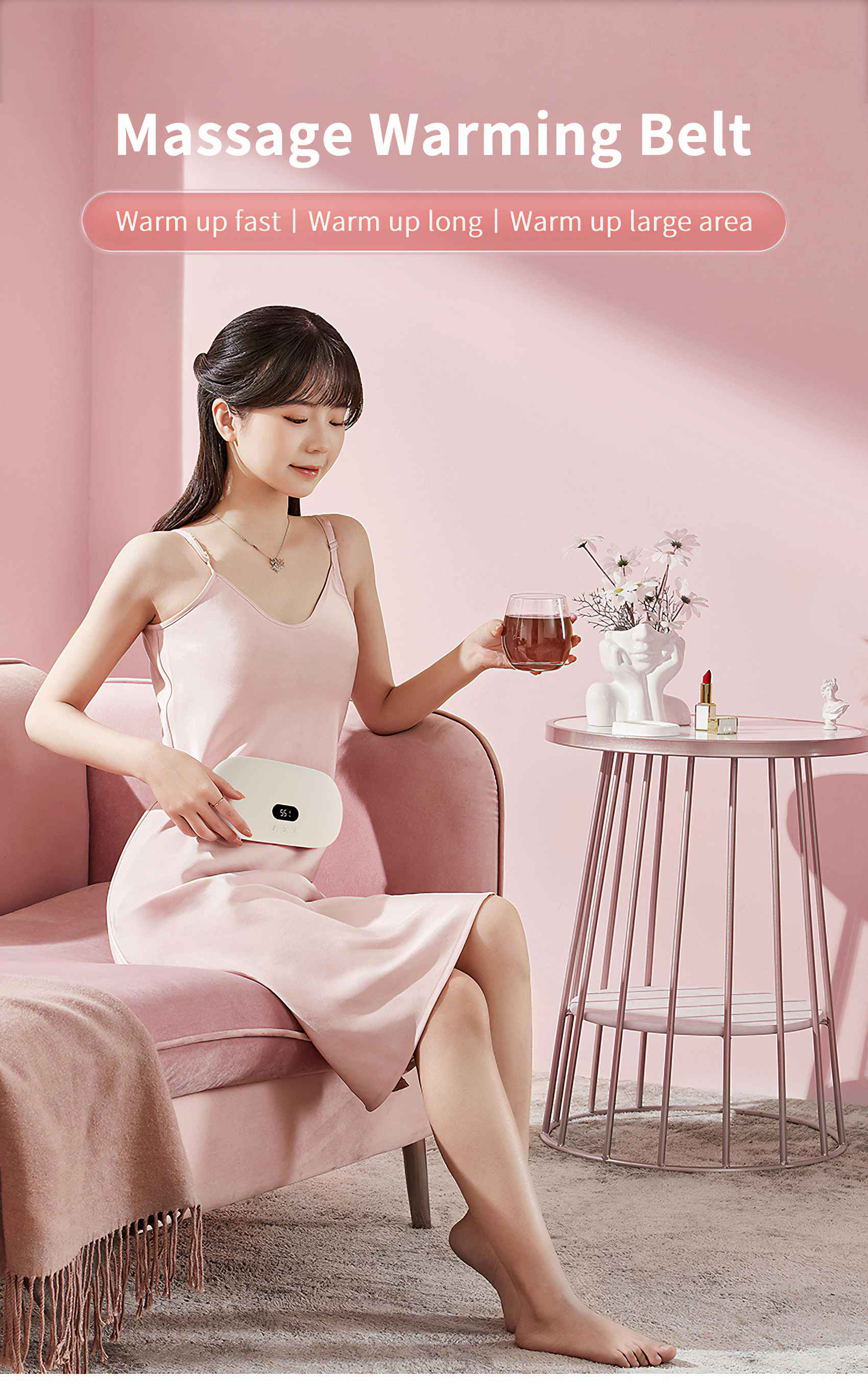 Frau in rosa Kleid mit Massagegürtel, hält ein Glas. Rosa Sofa und Tisch mit Blumen.