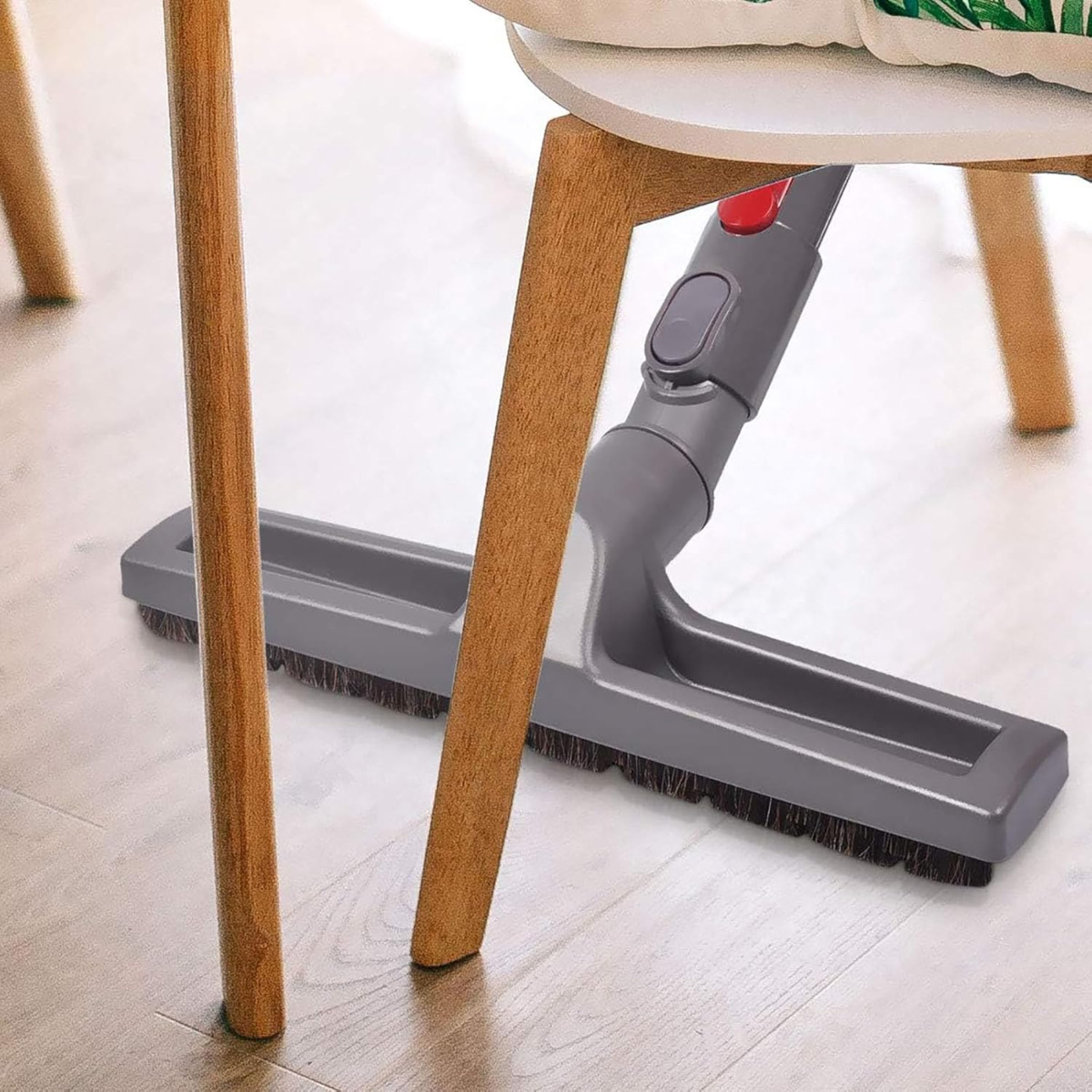 Ein grauer Staubsaugerkopf befindet sich unter einem weißen Stuhl. Holzstühle stehen auf einem Holzboden.