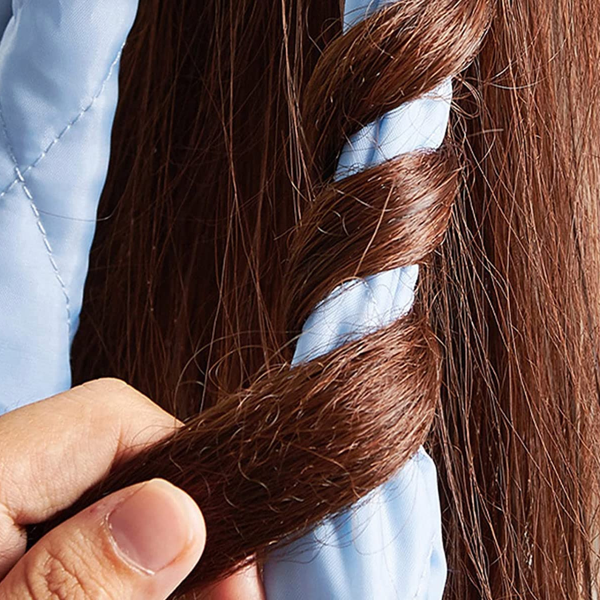 Eine Hand hält einen Zopf aus braunem Haar, der um einen hellblauen, gesteppten Haarwickler gewickelt ist. Der Hintergrund ist mehr braunes Haar.