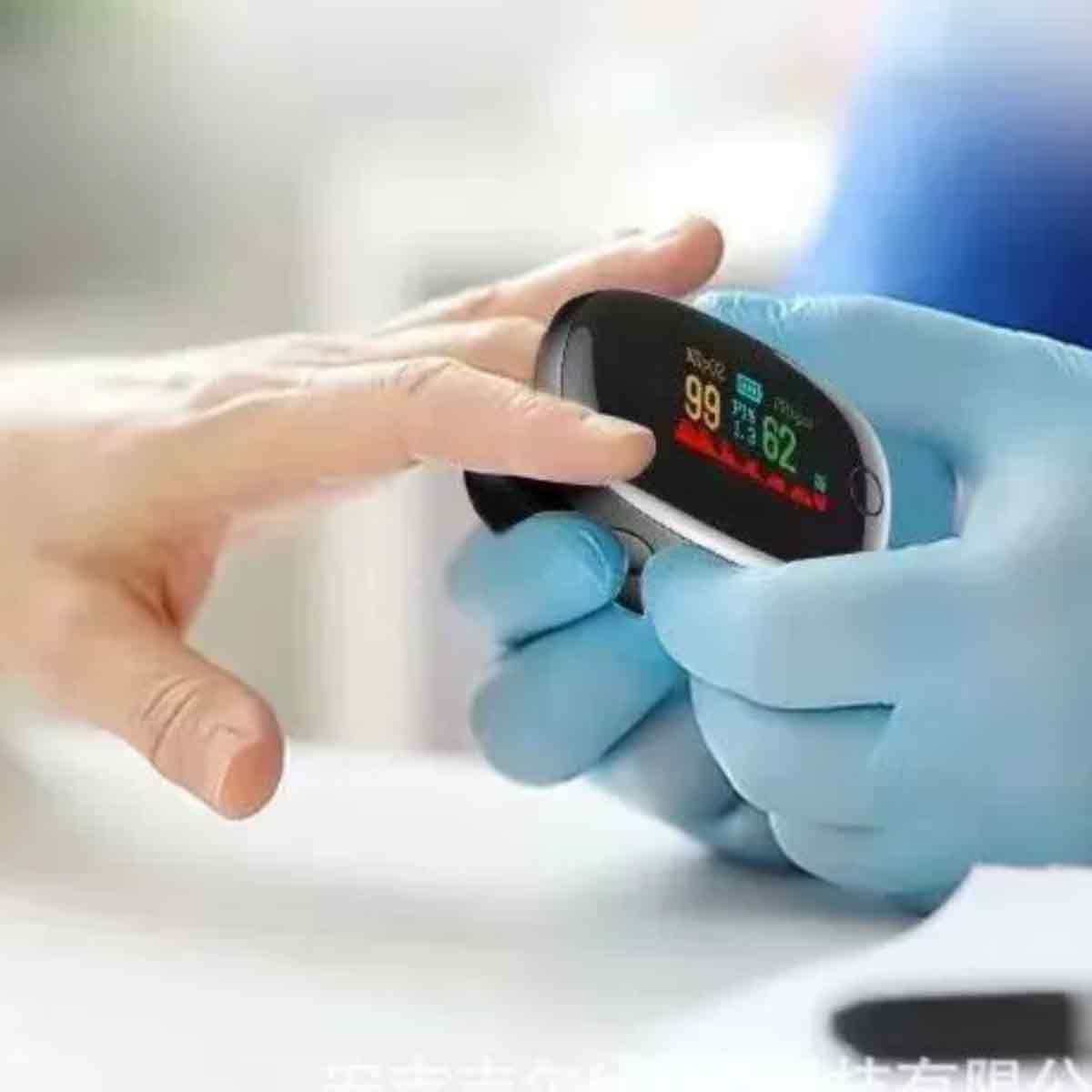 Ein Pulsoximeter misst am Finger 99% SpO2 und 62 bpm. Eine Hand mit blauen Handschuhen hält das Gerät.