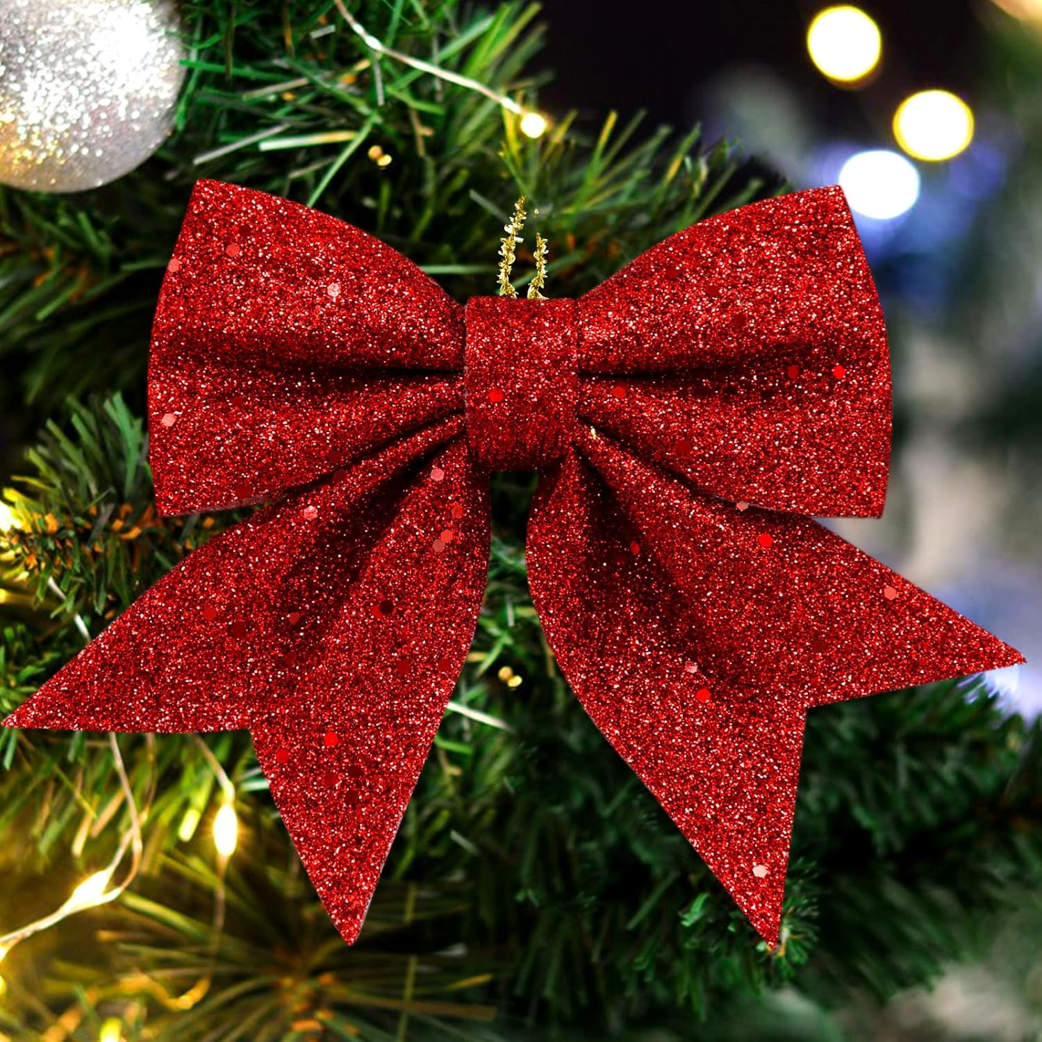 Eine glitzernde rote Schleife schmückt einen Weihnachtsbaum. Grüne Nadeln und weiche Lichter bilden den Hintergrund. Ein silberner Schmuck ist ebenfalls zu sehen.