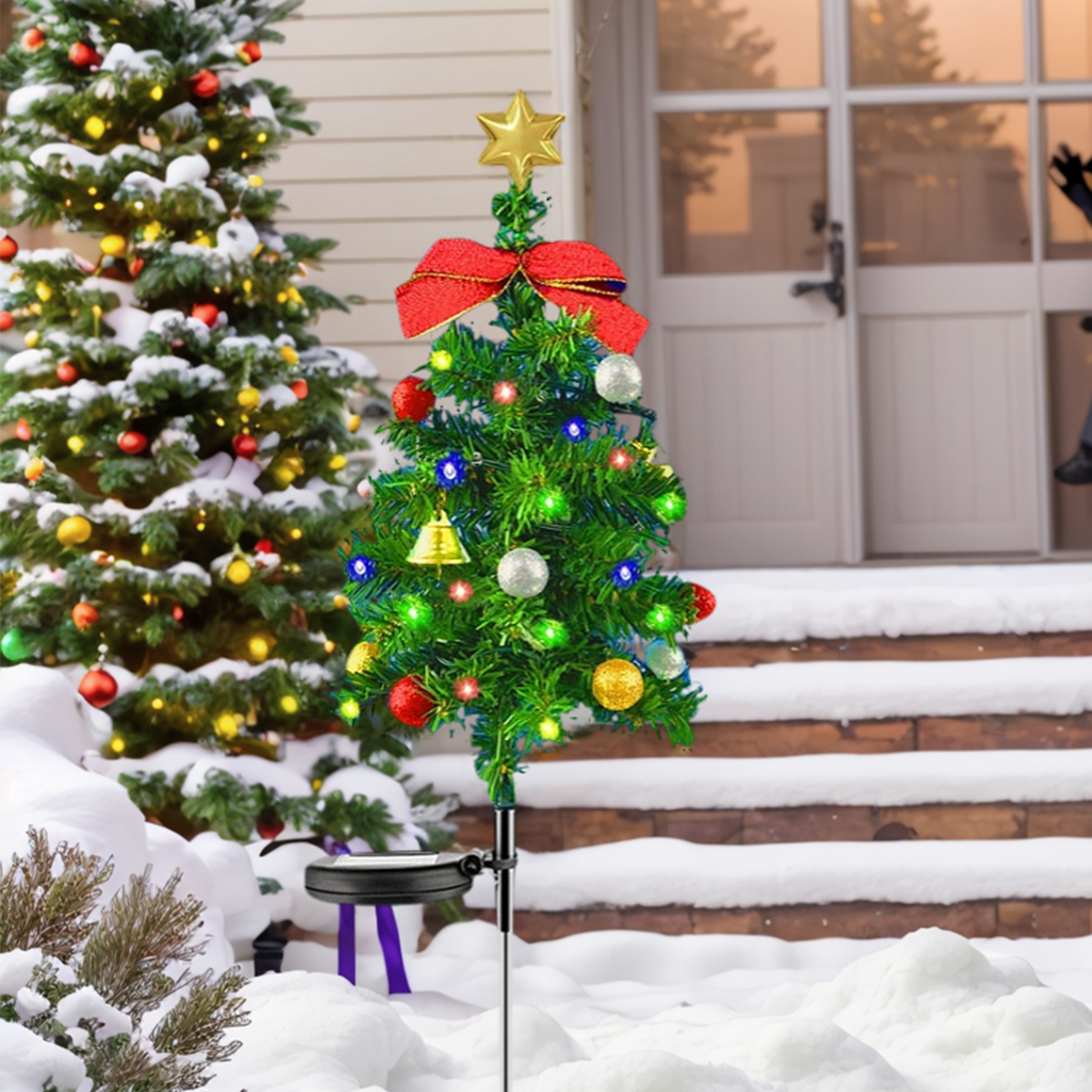 Ein kleiner, dekorierter Weihnachtsbaum mit Stern, roter Schleife und Ornamenten steht im Schnee. Dahinter steht ein größerer Baum.