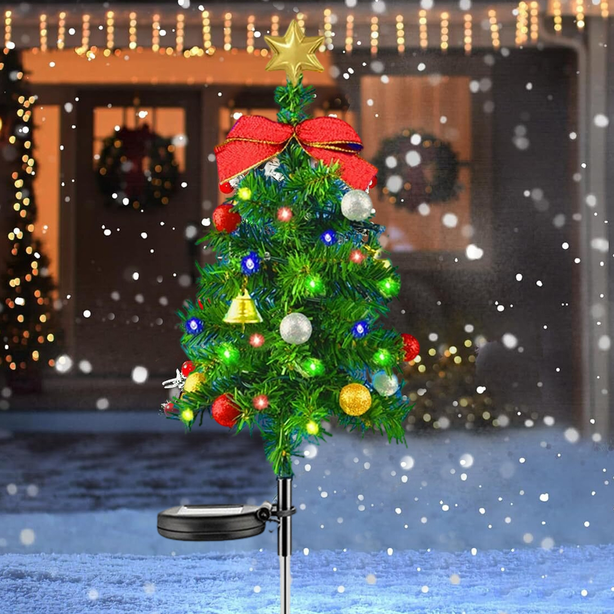 Eine kleine Weihnachtsbaumdekoration mit Lichtern, einem Stern und einer roten Schleife. Es schneit vor einem Haus.