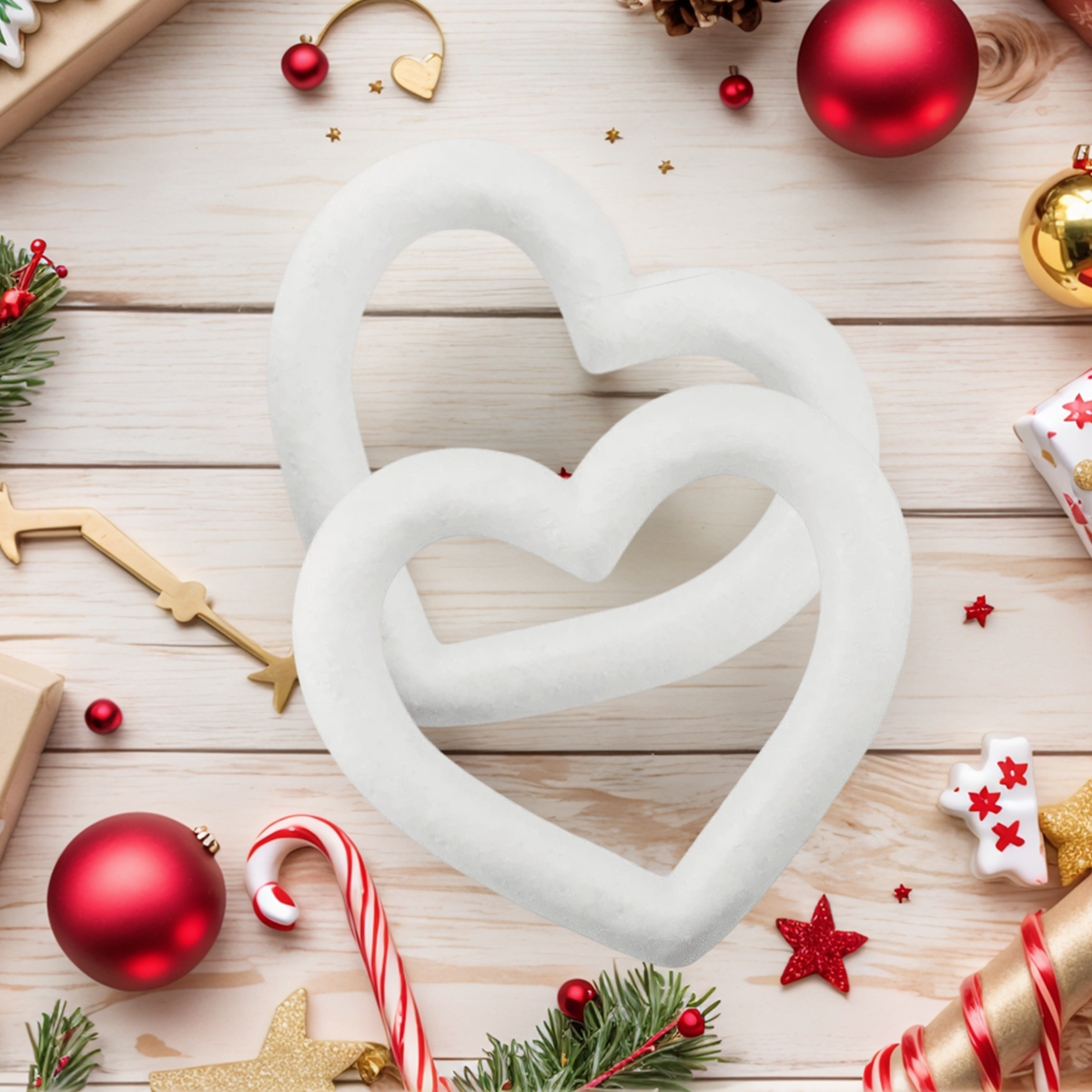 Zwei ineinander verschlungene weiße Herzformen, umgeben von Weihnachtsschmuck und Dekorationen auf hellem Holz.