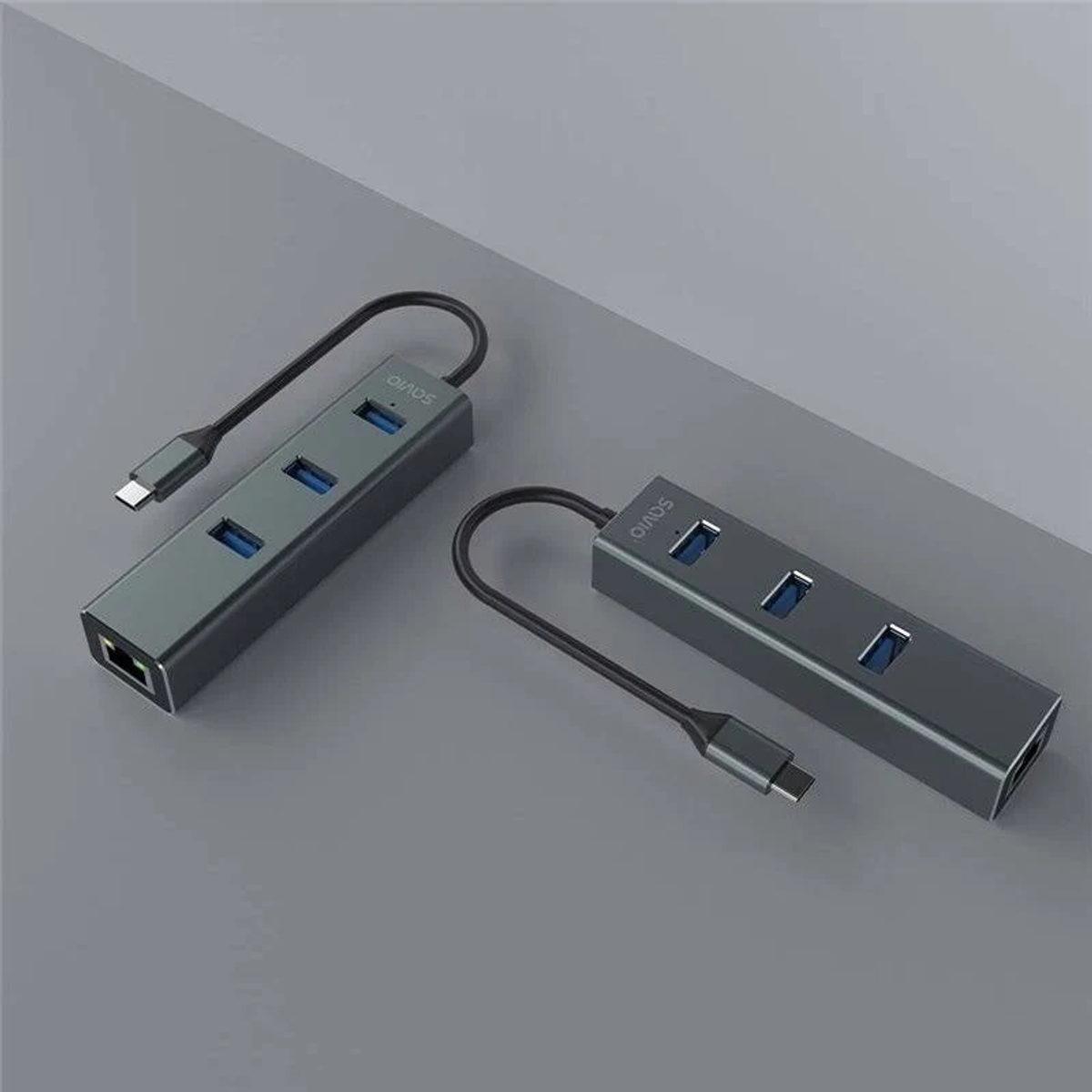 Zwei graue USB-Hubs mit schwarzen Kabeln und blauen USB-Anschlüssen auf einer grauen Oberfläche. Die Hubs sind mit 'SAVIO' gekennzeichnet.