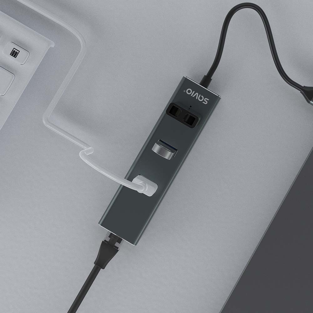 Ein grauer USB-Hub mit mehreren Anschlüssen und angeschlossenen Kabeln. Im Hintergrund befindet sich eine weiße Tastatur. Der Hub ist mit 'SAVIO' beschriftet.