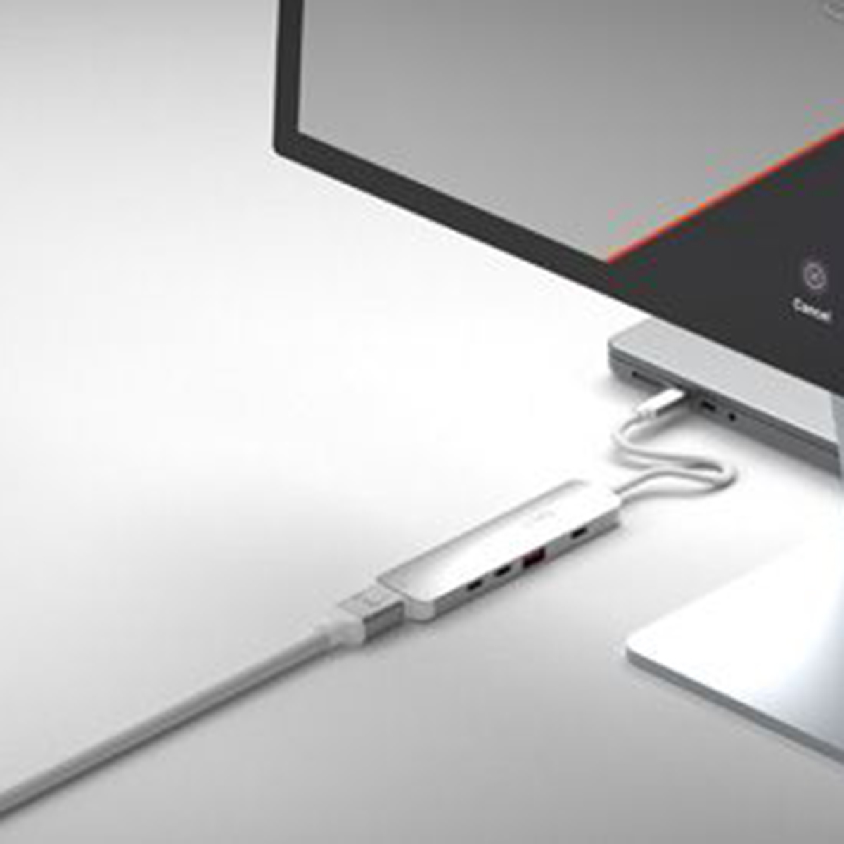Ein silberner USB-C-Hub, der mit einem Laptop und einem Monitor verbunden ist. Der Hub hat mehrere Anschlüsse. Alles befindet sich auf einer weißen Oberfläche.