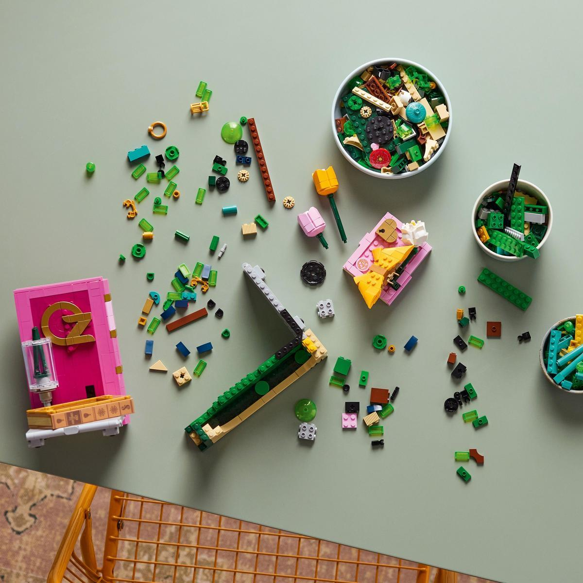 Bovenaanzicht van Lego-stenen verspreid over een groen oppervlak. Bevat roze en gele Lego-creaties en kommen gevuld met kleurrijke stenen.
