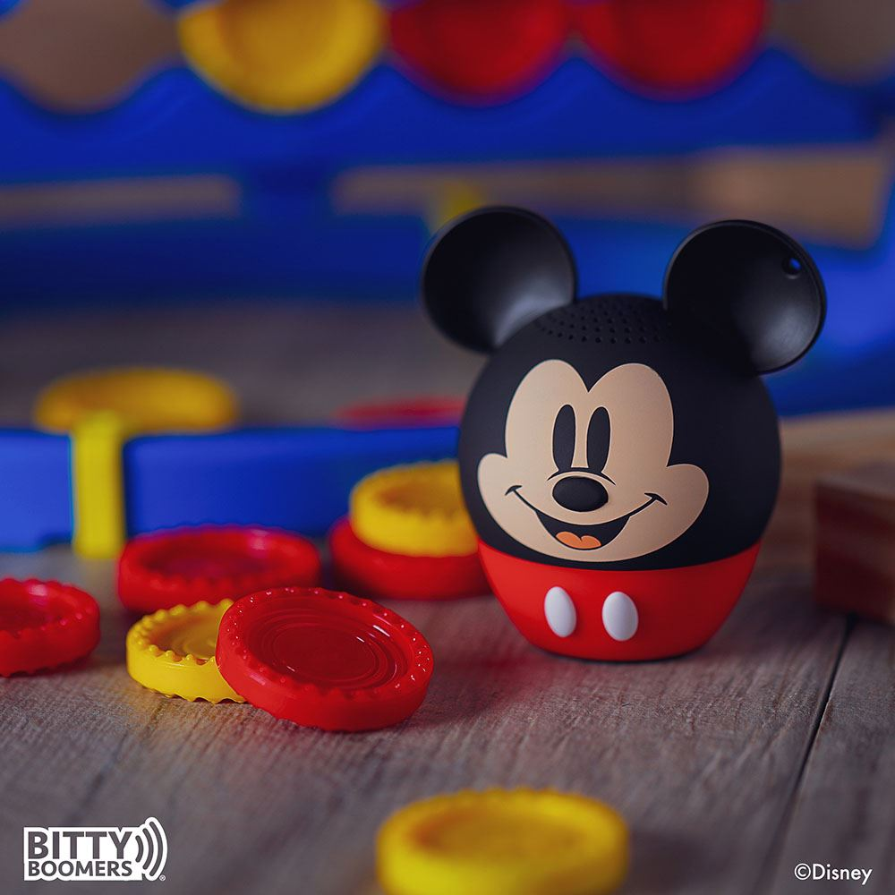 Un altoparlante a forma di Topolino è su una superficie di legno. Tappi rossi e gialli e sfondo blu sono nella scena. Logo Disney.