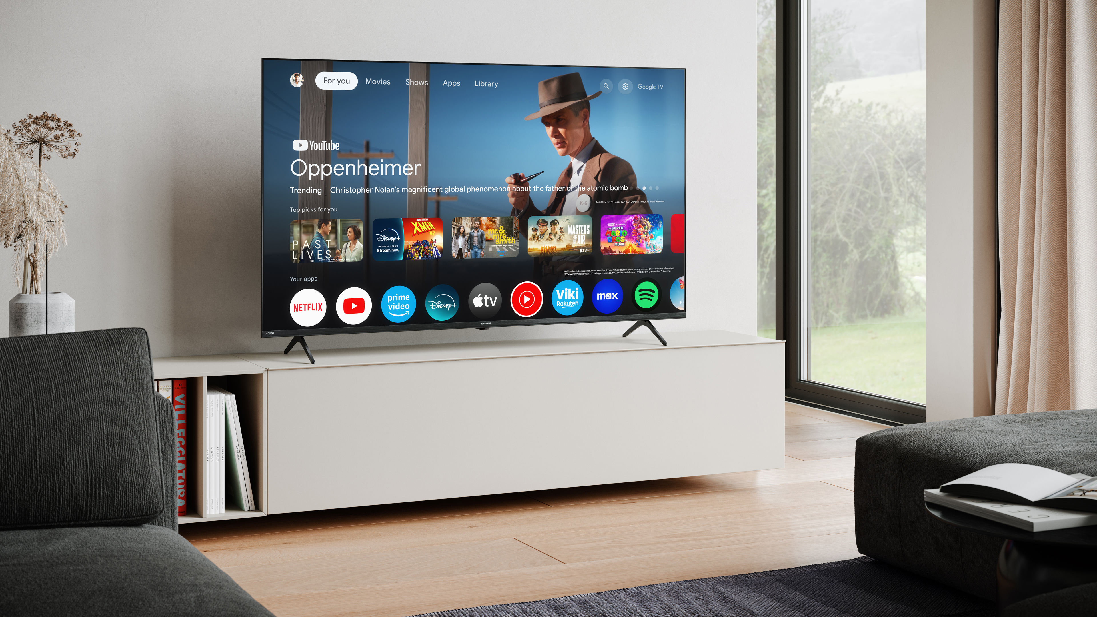 A TV displays a movie, Oppenheimer. A white cabinet holds the TV. A couch and window are on the sides.