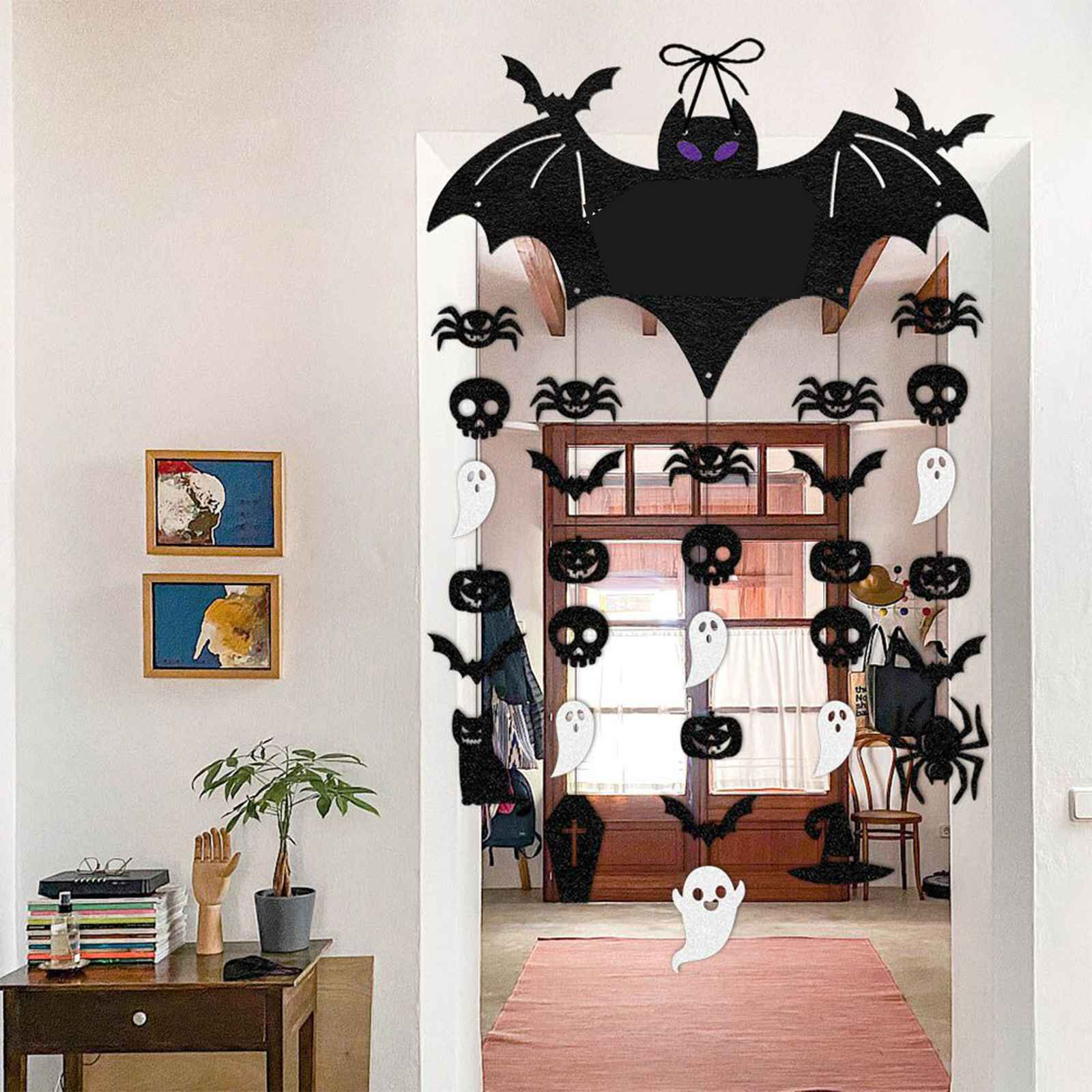 Eine Halloween-Dekoration hängt in einem Türrahmen. Sie zeigt Fledermäuse, Spinnen, Kürbisse, Totenköpfe und Geister. Links ein Tisch.